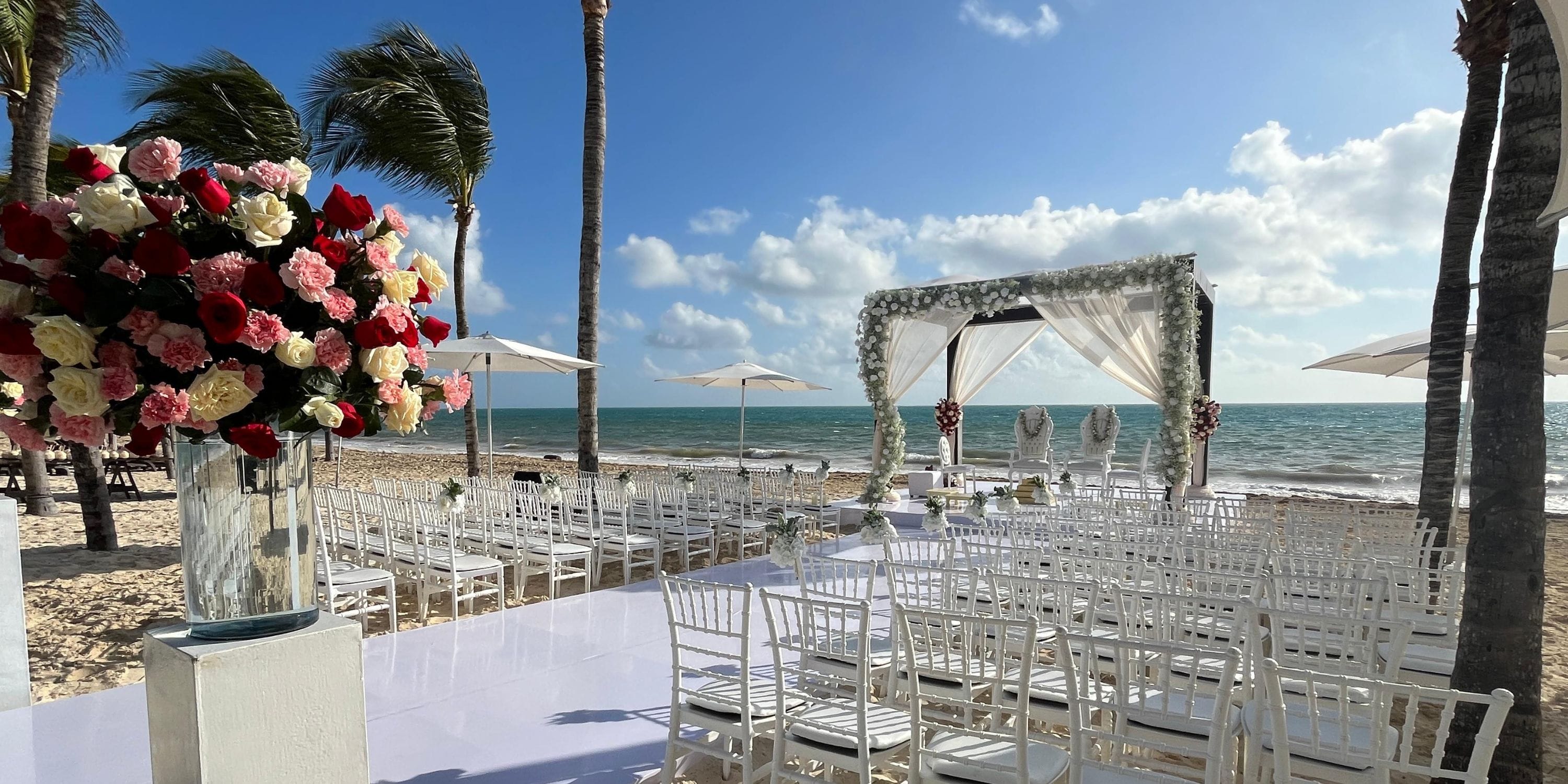 Destination wedding at Royalton Riviera Cancun featuring white chairs, floral arrangements, and ocean views.