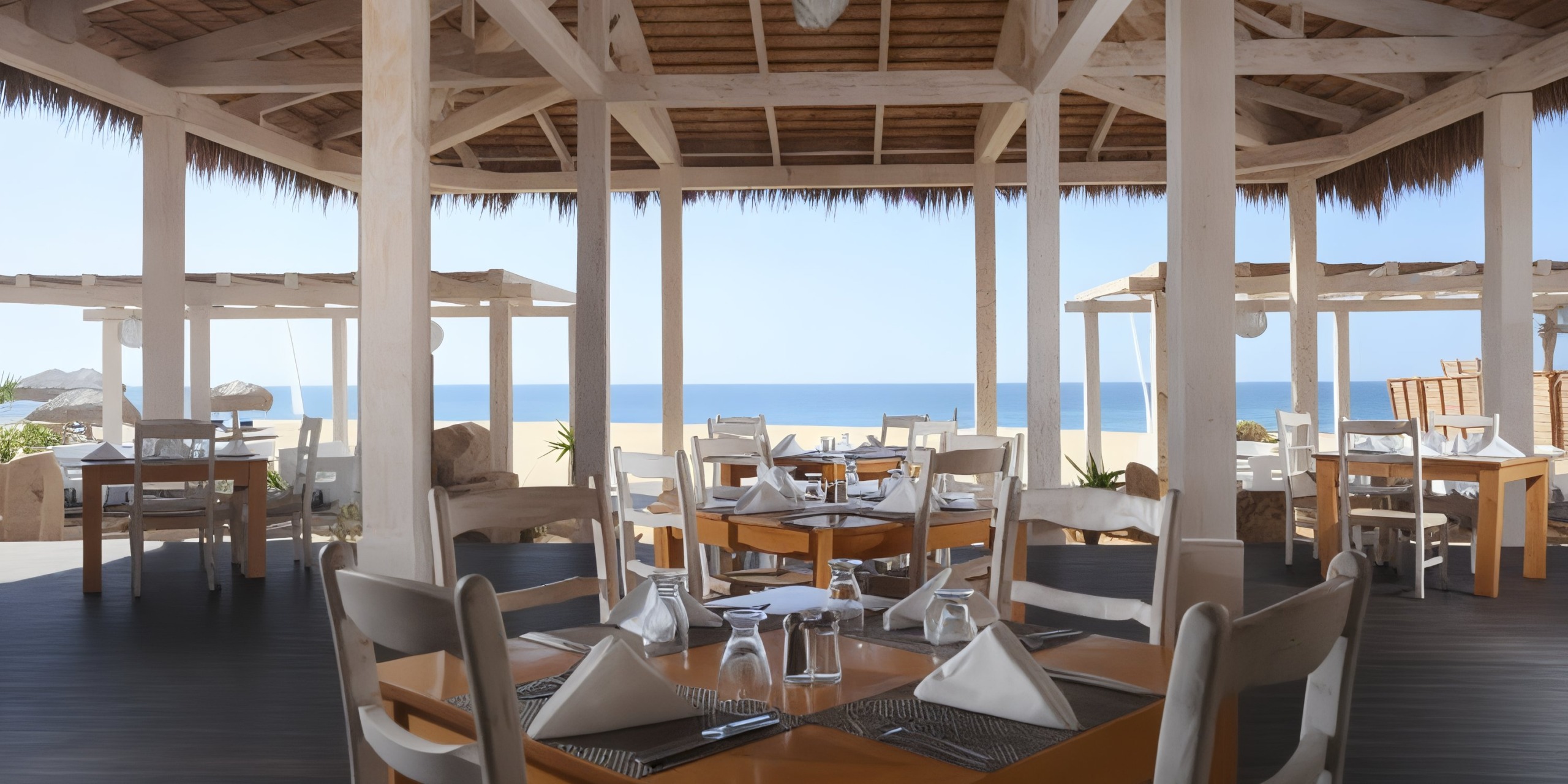 Dine at the open-air beachside restaurant of Sandos Finisterra Los Cabos, where wooden tables and chairs are set for a delightful meal with a stunning ocean view in the background.