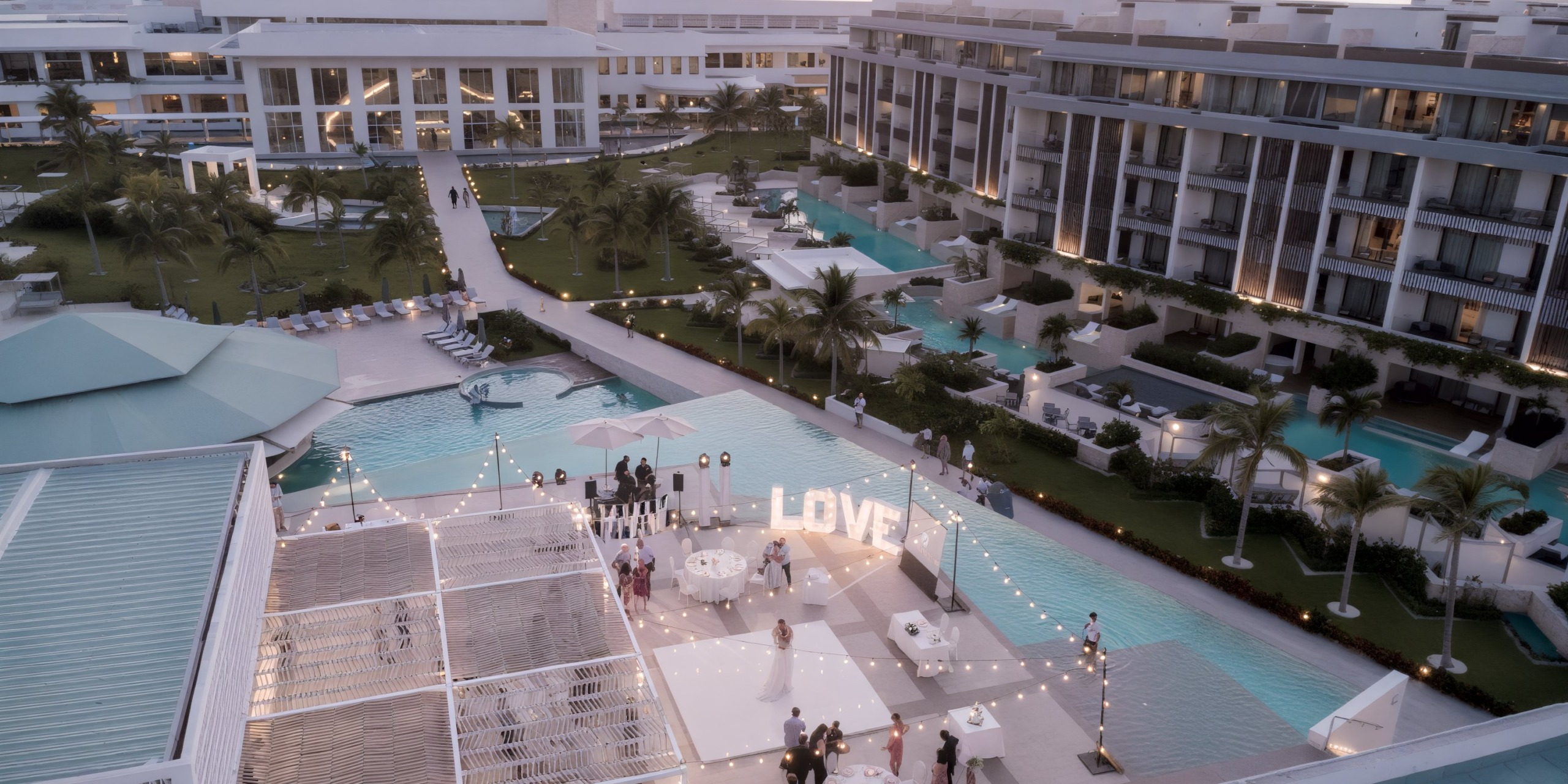 A breathtaking aerial view of the Majestic Elegance Costa Mujeres pool, beautifully adorned with a "LOVE" sign and glistening string lights, creating a perfect setting for a destination wedding.