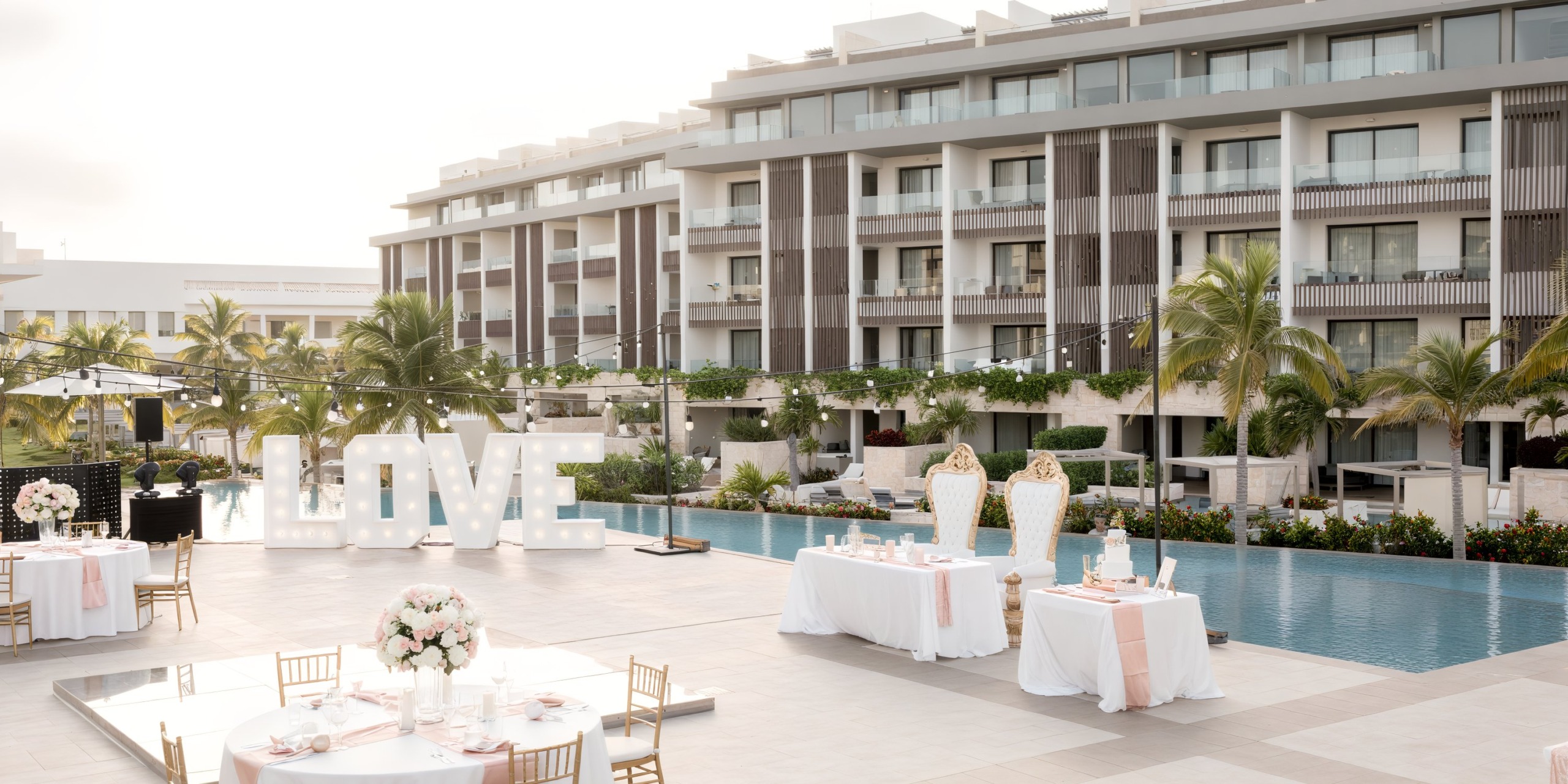 Majestic Elegance Costa Mujeres offers a picturesque destination wedding setup, featuring a beautiful "LOVE" sign strategically placed by the pool and the resort building.