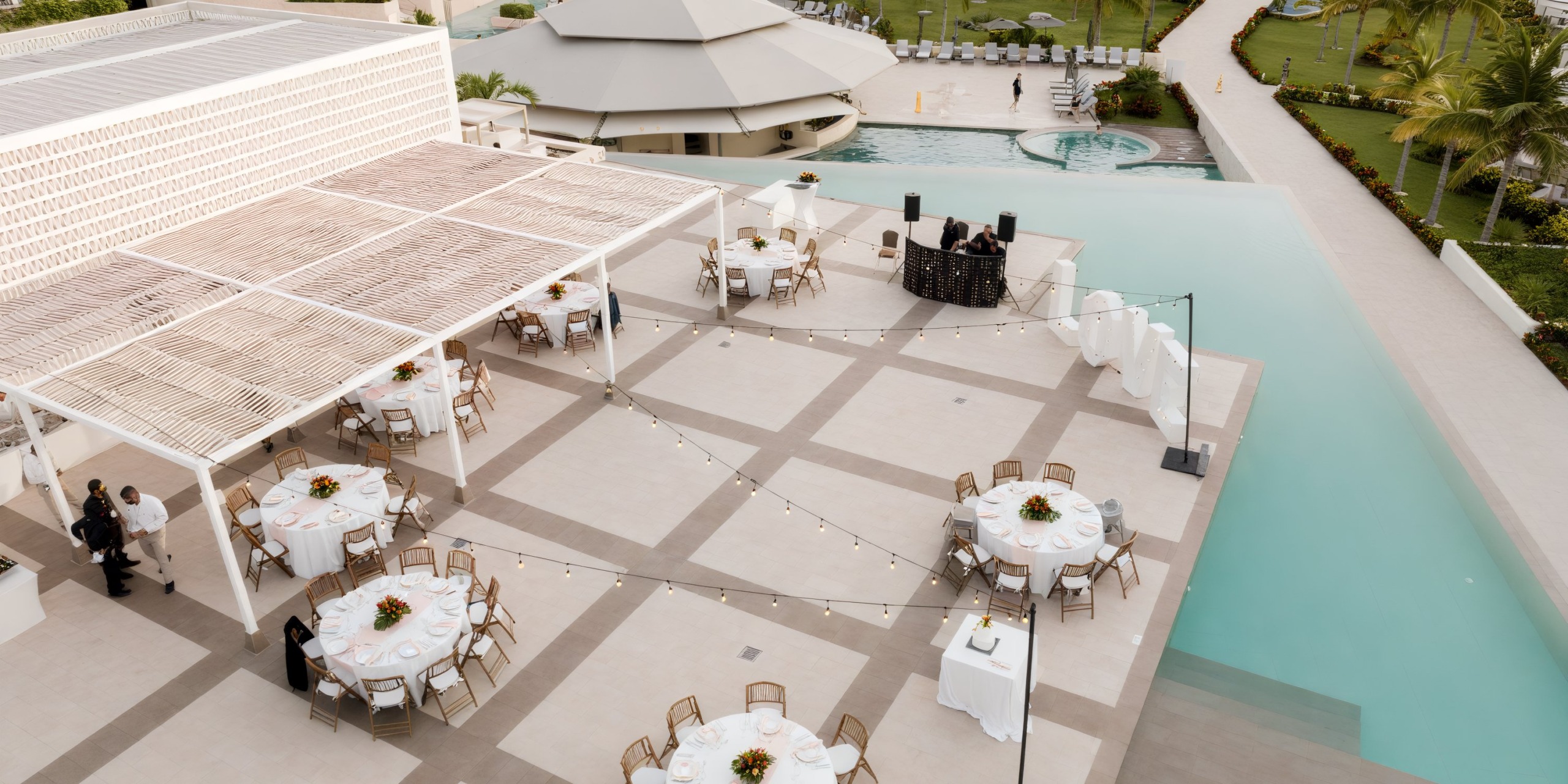 Majestic Elegance Costa Mujeres offers an enchanting outdoor space perfect for a destination wedding, featuring round tables adorned with string lights and a stunning pool view.