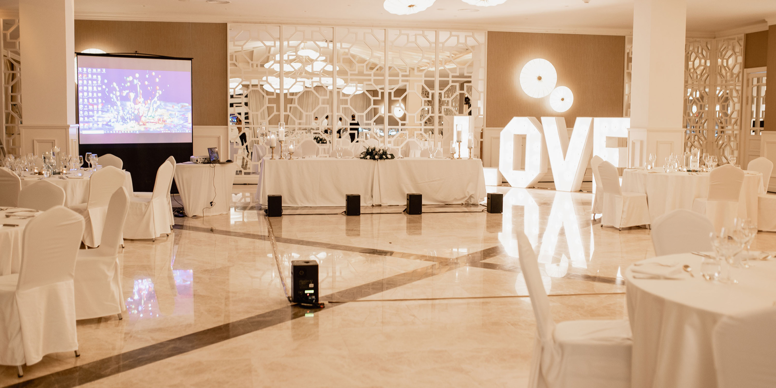 Elegant Majestic Elegance Costa Mujeres wedding reception hall decorated with white linens, large "love" sign, and a video screen.