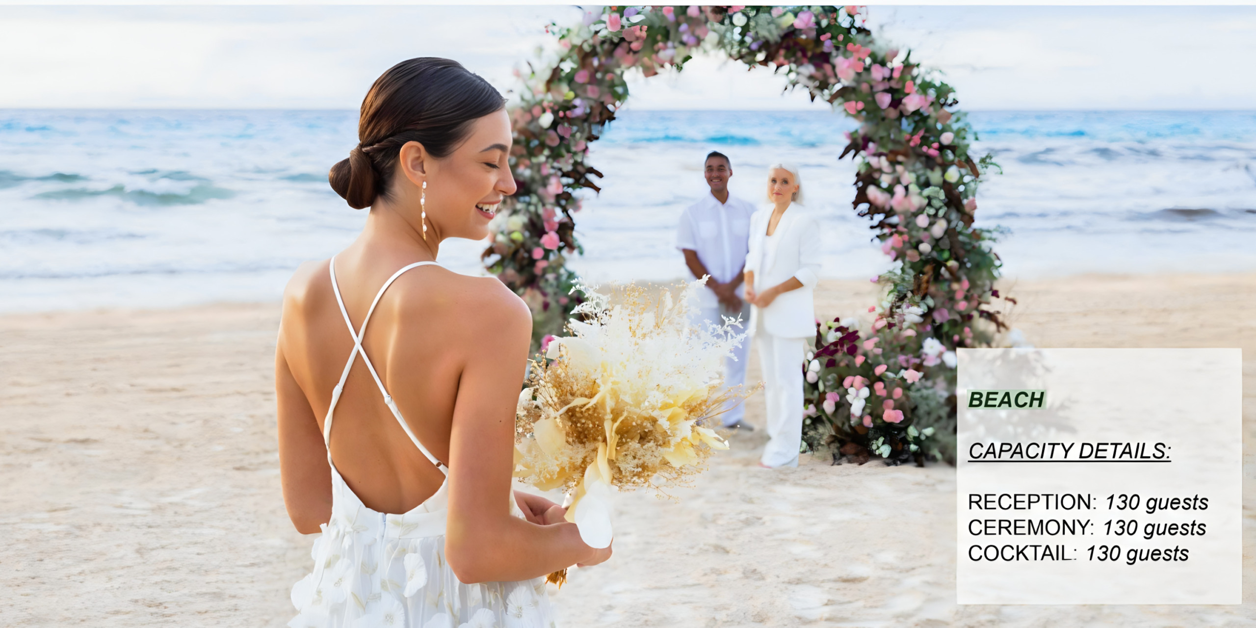 A bride holding a bouquet walks toward a wedding arch with a couple in the background at a destination wedding on a beach.