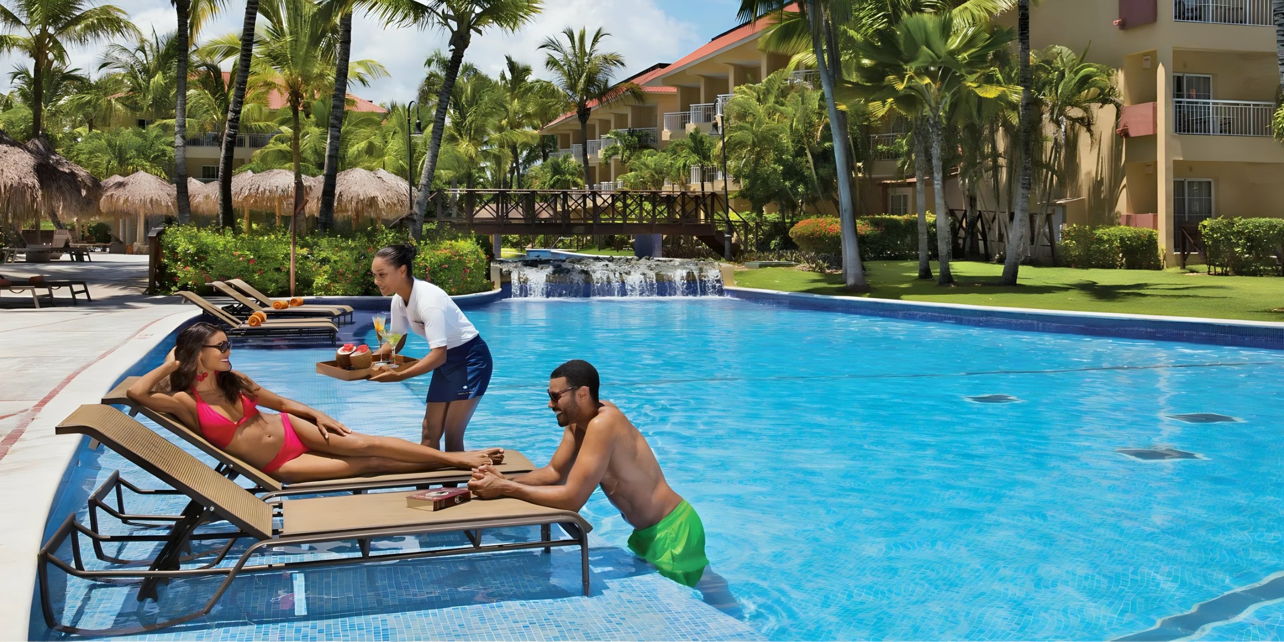 Beautiful couple lounges poolside being waited on by a waitress attendant at the Dreams Punta Cana pool