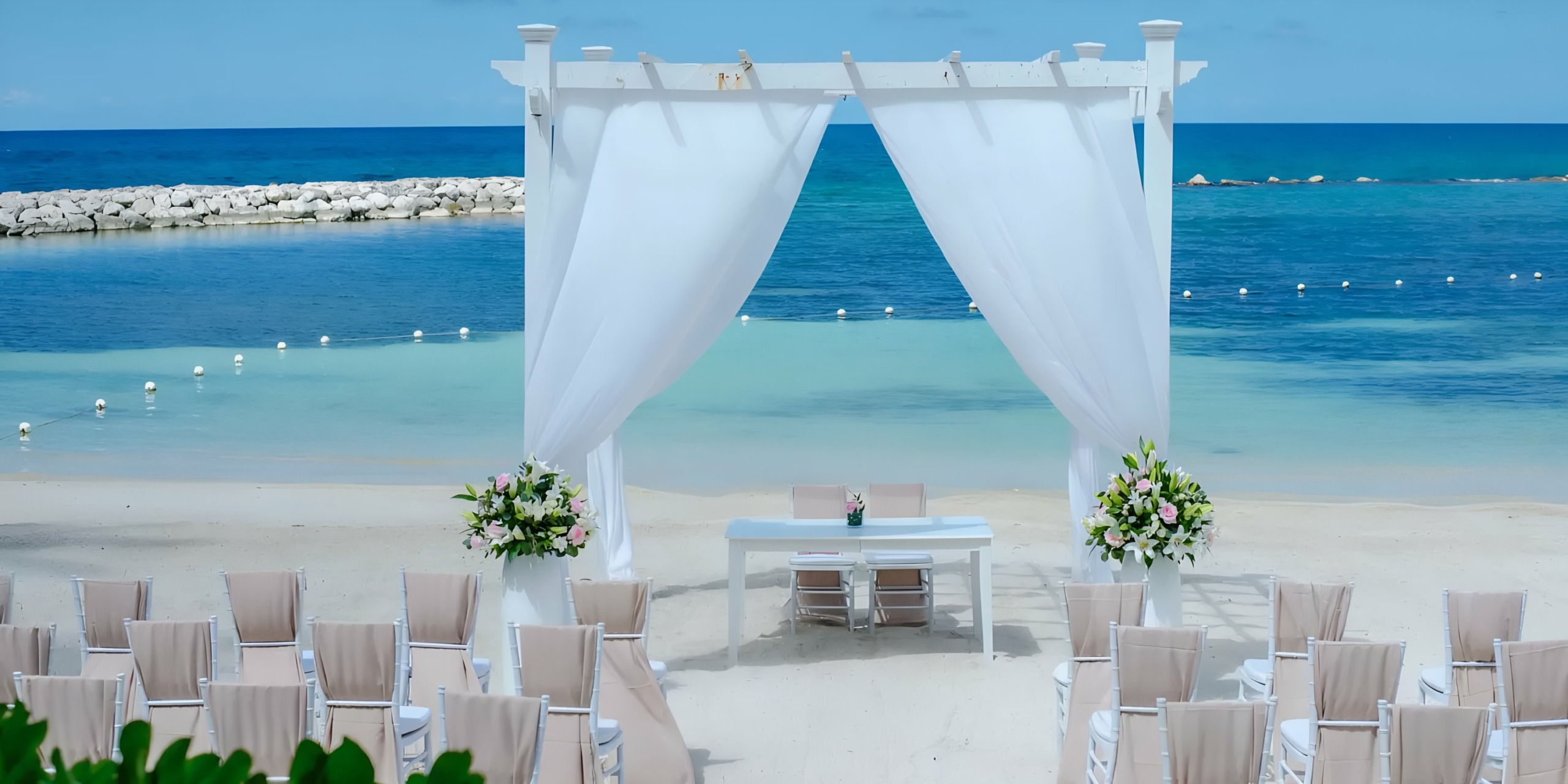 Beach wedding ceremony setup at **Grand Palladium Lady Hamilton** with white chairs, an arch, and a view of the ocean.
