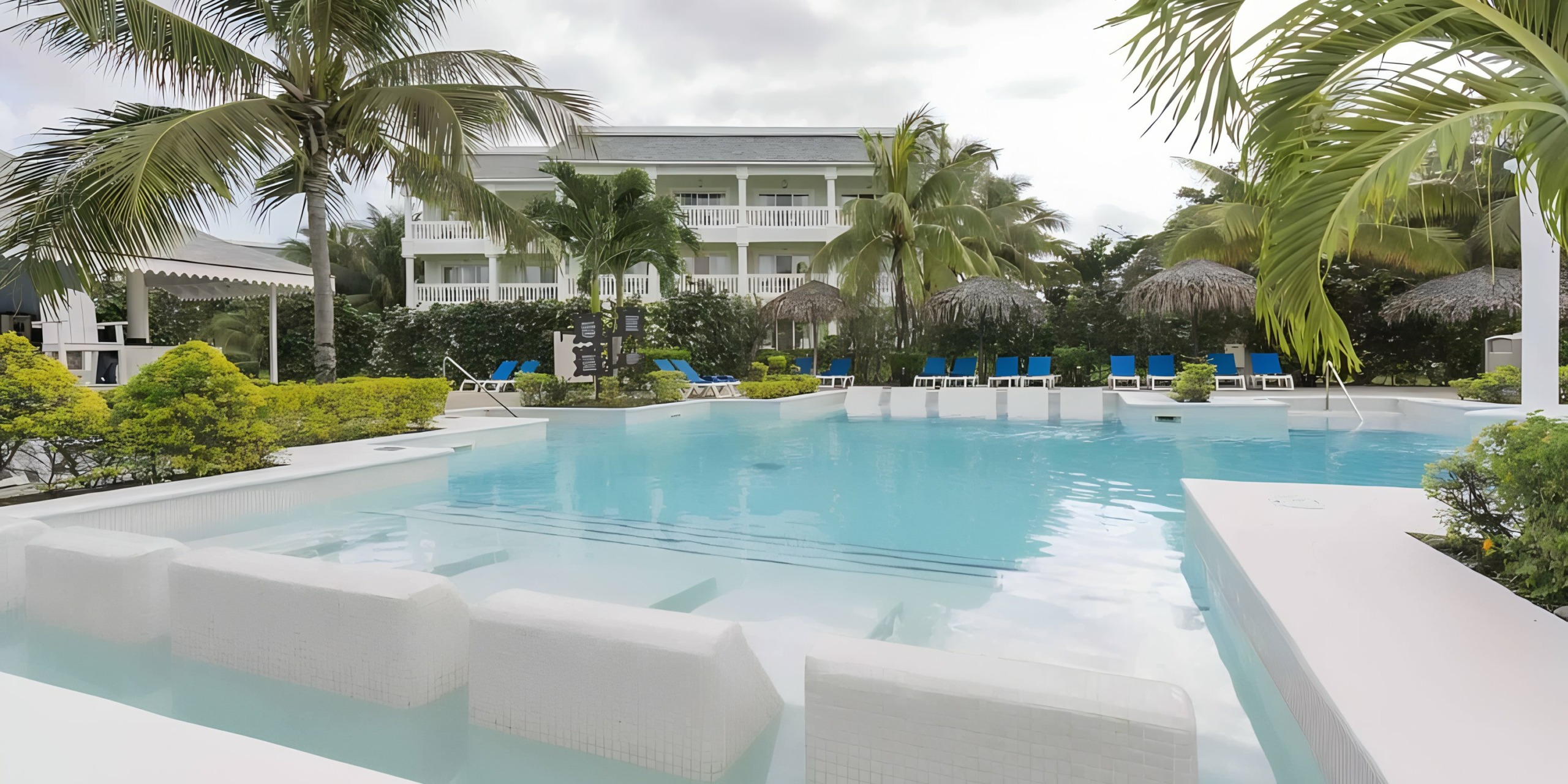A large resort-style pool with chairs and palm trees under a cloudy sky at the Grand Palladium Lady Hamilton Resort, perfect for a destination wedding at the Grand Palladium Lady Hamilton.