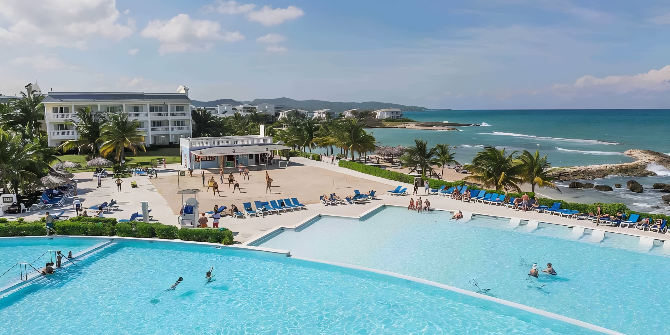 A coastal resort view featuring a large swimming pool, sunbathers, and a clear blue sky at the Grand Palladium Lady Hamilton.