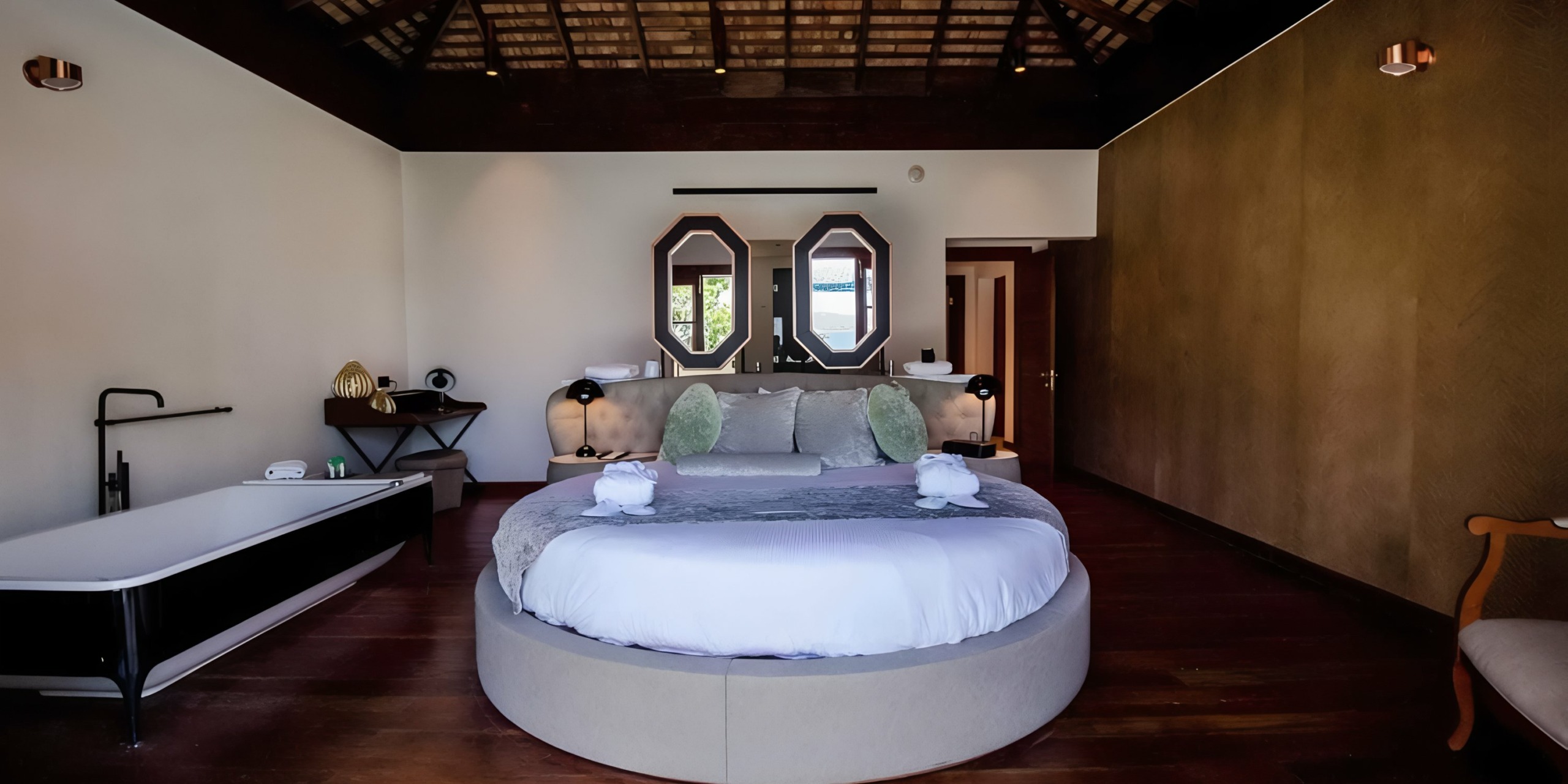 A spacious, modern bedroom with a round bed, unique mirror design, and dark wood elements perfect for a Grand Palladium Lady Hamilton wedding.