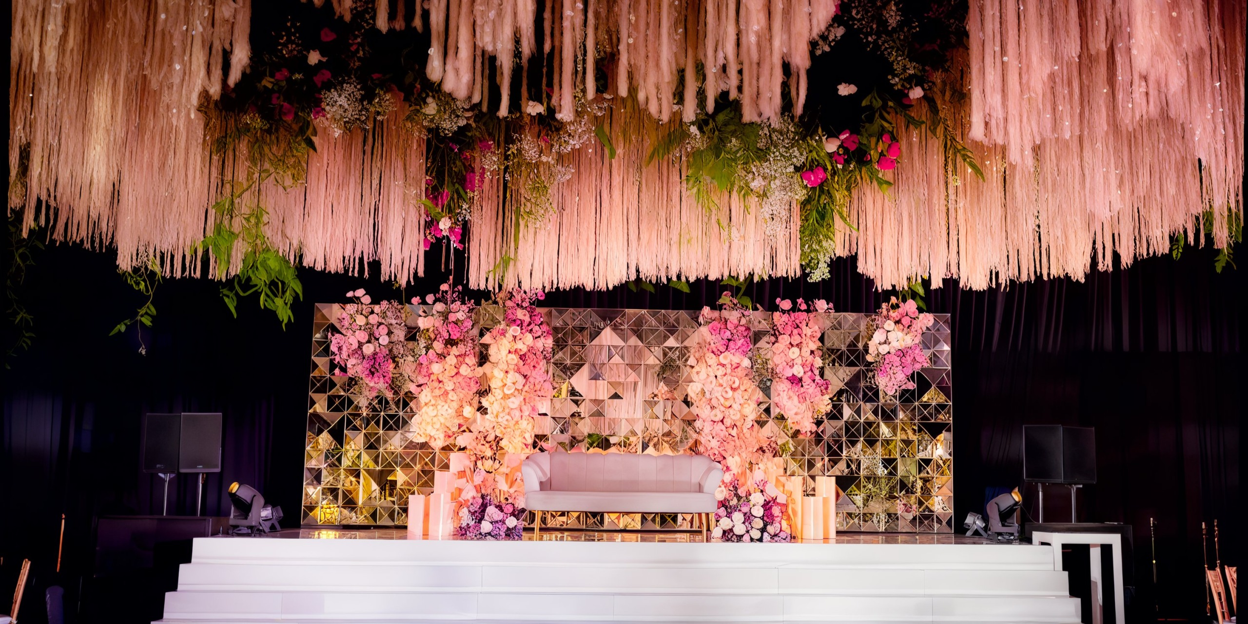 A stage at the Grand Palladium Costa Mujeres, featuring a white platform with a floral backdrop adorned with hanging flowers and greenery.