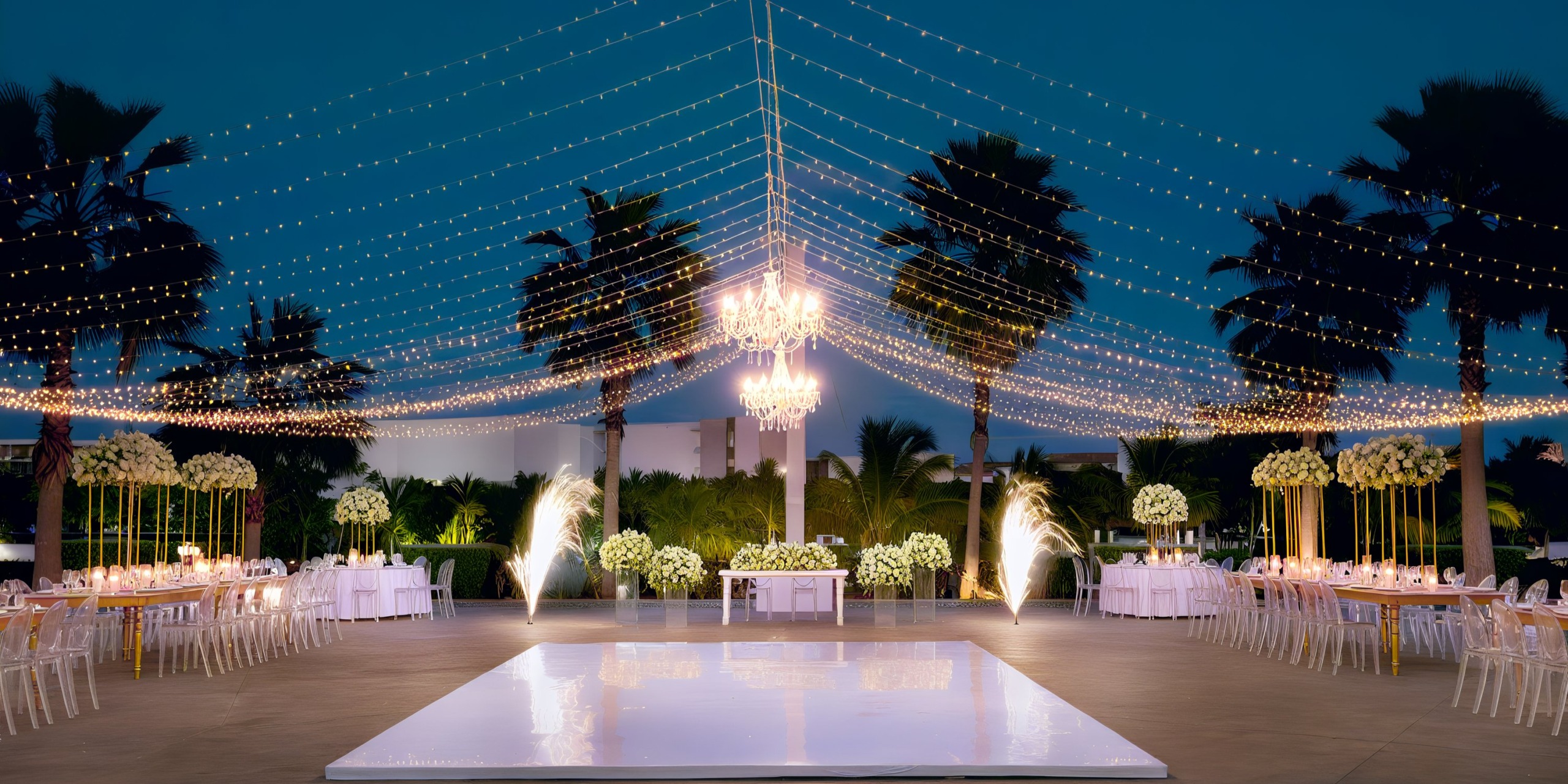 An outdoor wedding setup at the Grand Palladium Costa Mujeres includes a glossy dance floor, enchanting string lights overhead, elegant palm trees, beautiful flower arrangements, dining tables ready for guests, and a stunning chandelier.