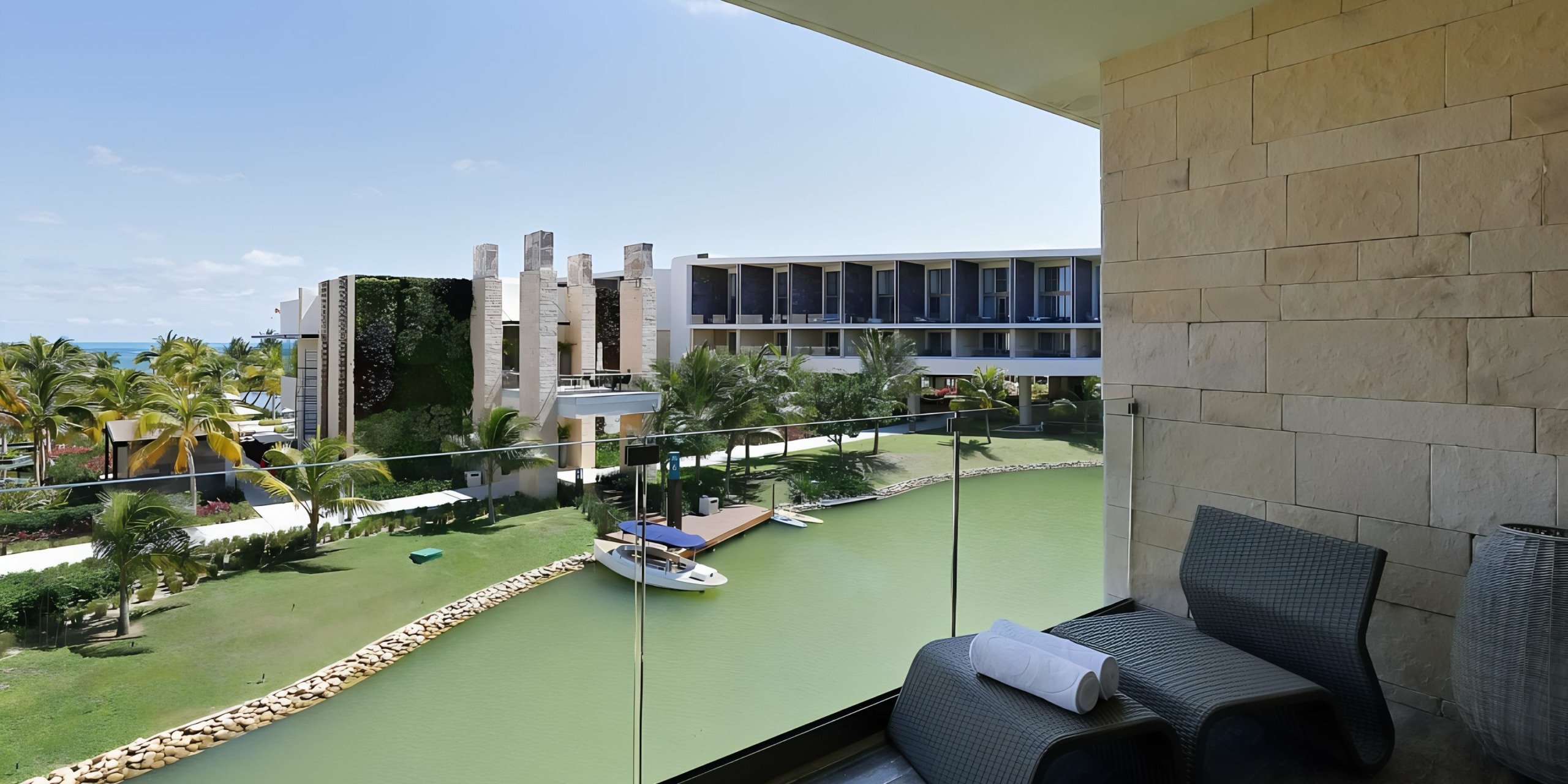 View from a balcony overlooking the Grand Palladium Costa Mujeres with landscaped grounds and a canal with a boat.