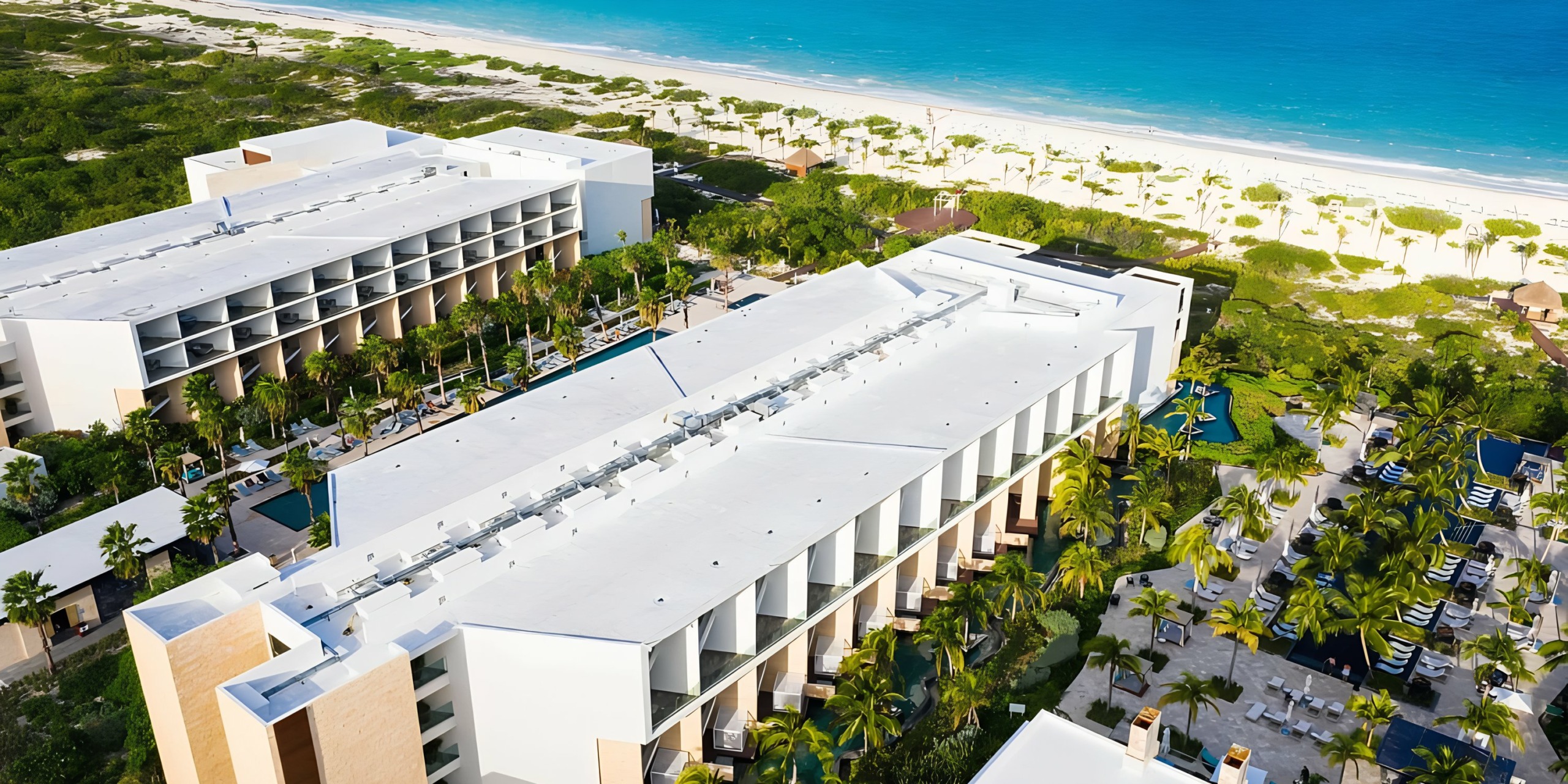 Aerial view of the Grand Palladium Costa Mujeres beachfront resort with palm trees and pools.