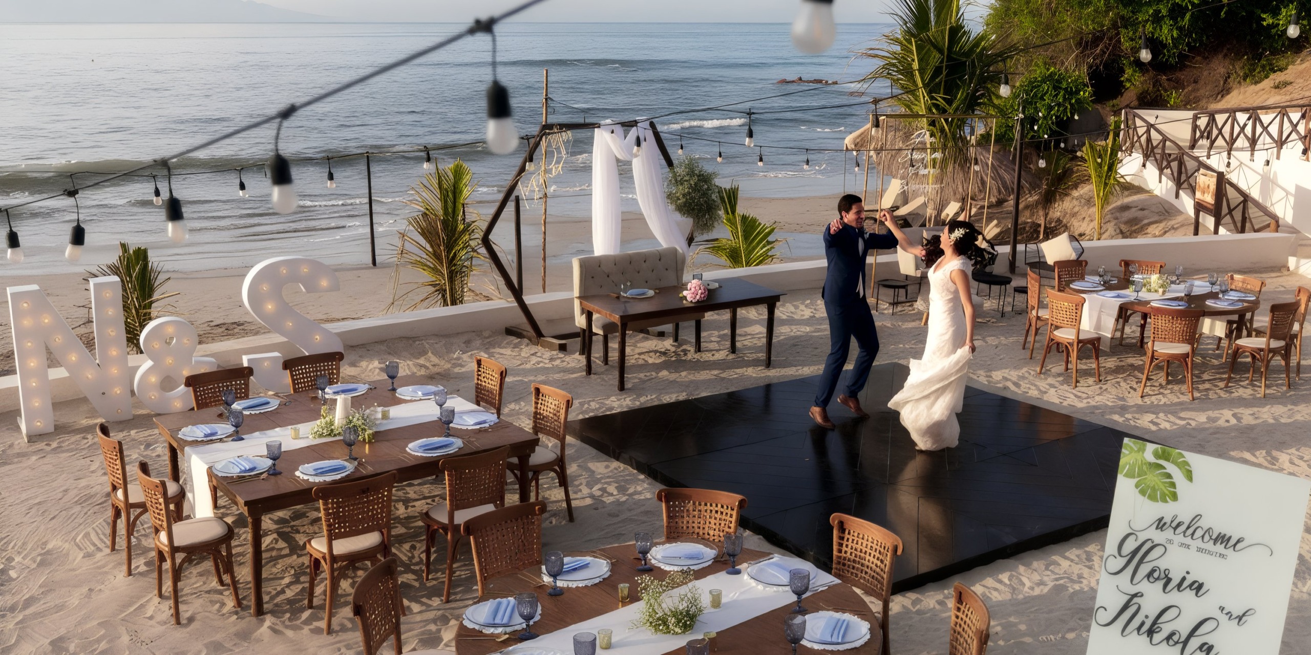 Bride and groom dancing on a beachside platform at Grand Palladium Vallarta, surrounded by decorated tables, the sea in the background, and large illuminated initials "N & S" on the sand.