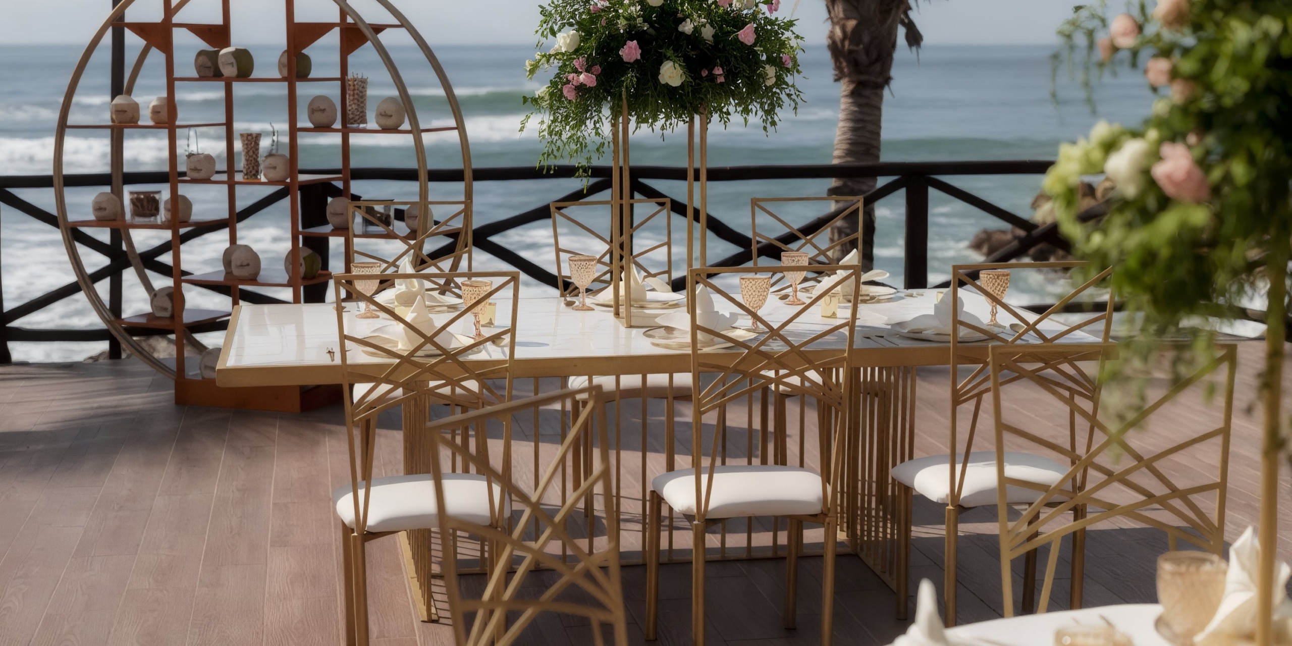 Experience an elegant outdoor dining setup at the Grand Palladium Vallarta, featuring a pristine white table, luxurious gold chairs, and a beautiful floral centerpiece. Enjoy stunning ocean views and picturesque palm trees in the background.