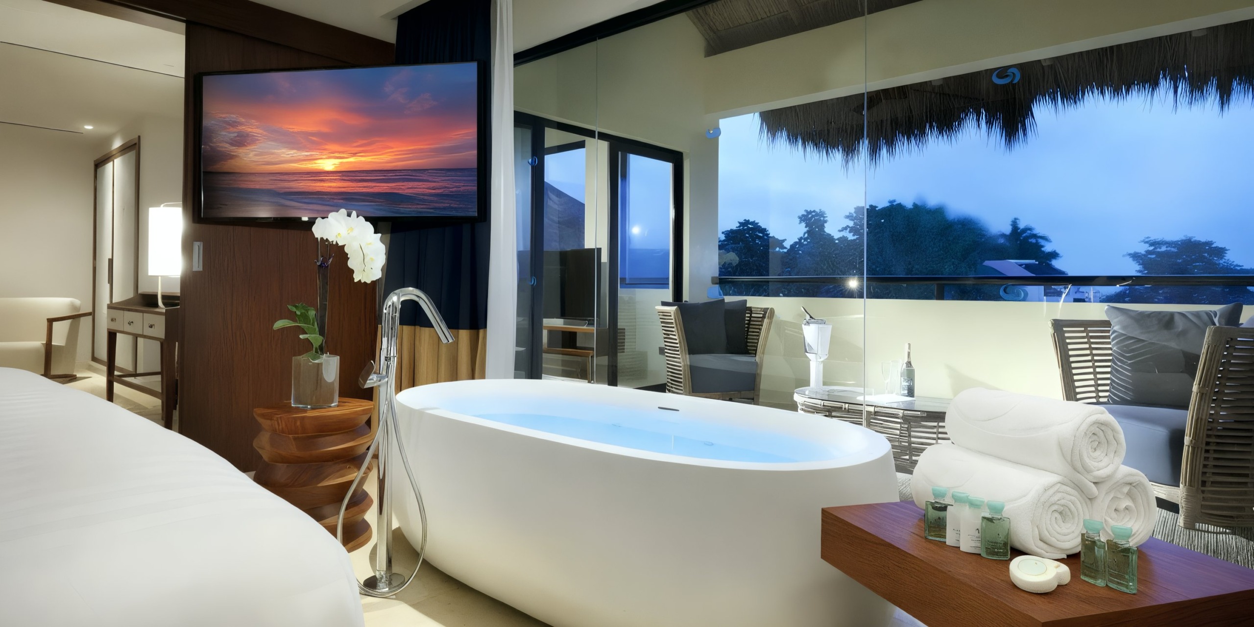 Experience opulence at the Grand Palladium Vallarta, featuring a luxurious room with a standalone bathtub, expansive windows offering tropical views, a wall-mounted TV for entertainment, and rolled towels along with toiletries elegantly arranged on a wooden table.