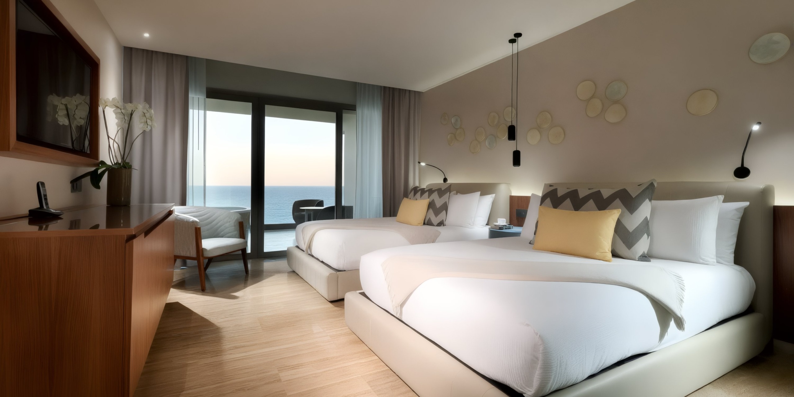 Stay at the Grand Palladium Costa Mujeres in a hotel room featuring two double beds, light wood flooring, a small desk with a chair, and large windows adorned with sheer curtains that offer breathtaking views of the ocean at sunset.