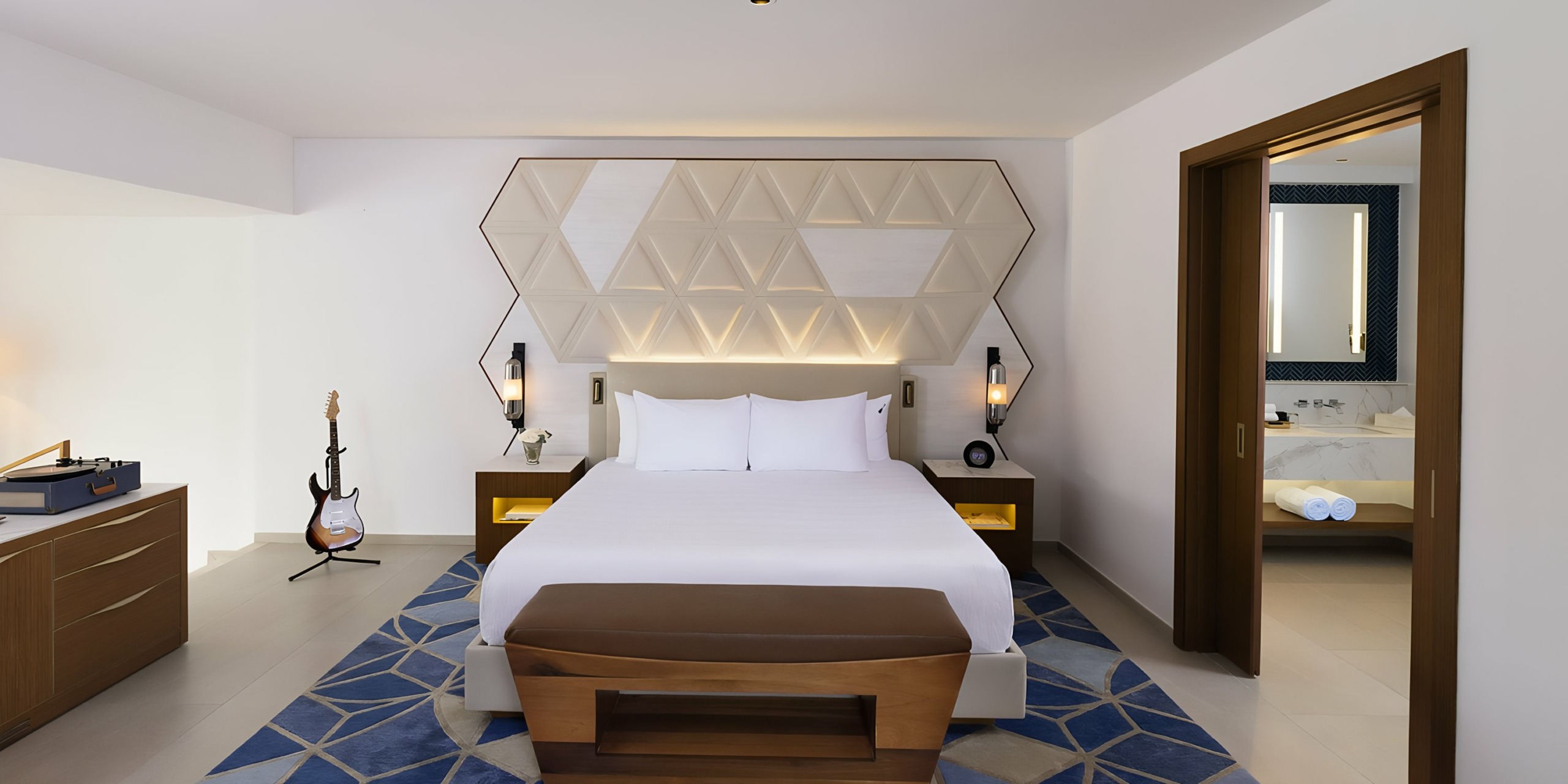 Modern hotel room at Hard Rock Punta Cana with geometric headboard design, guitar on stand, and bathroom visible through open door.