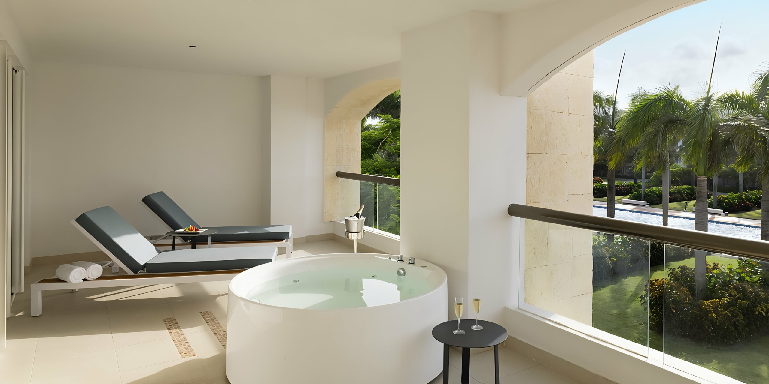Spacious modern bathroom at Hard Rock Punta Cana with a circular tub, lounging chairs, and a view of greenery.