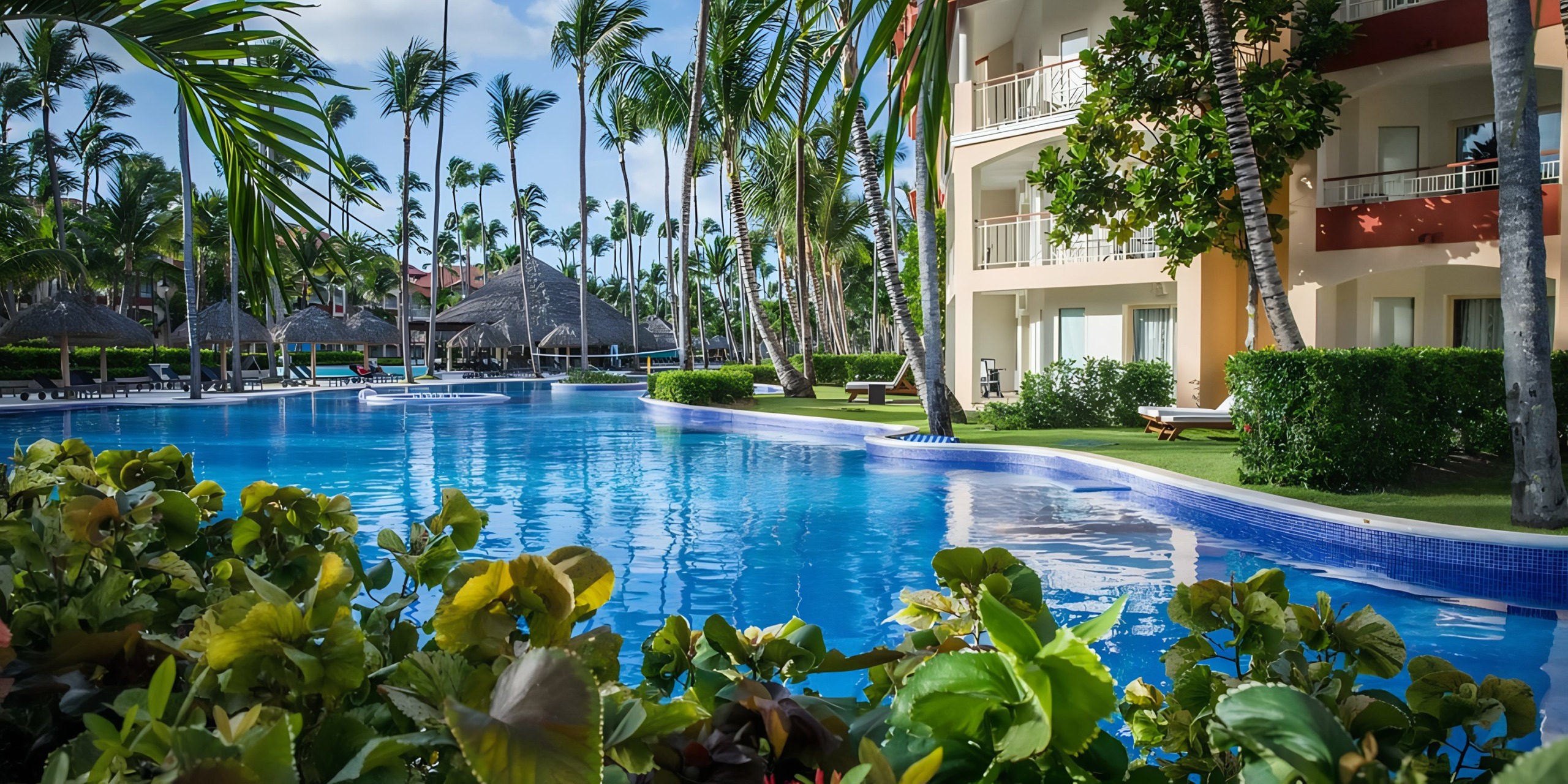 A serene resort pool surrounded by lush palm trees and flanked by multi-storied accommodations with balconies at Majestic Elegance Punta Cana.