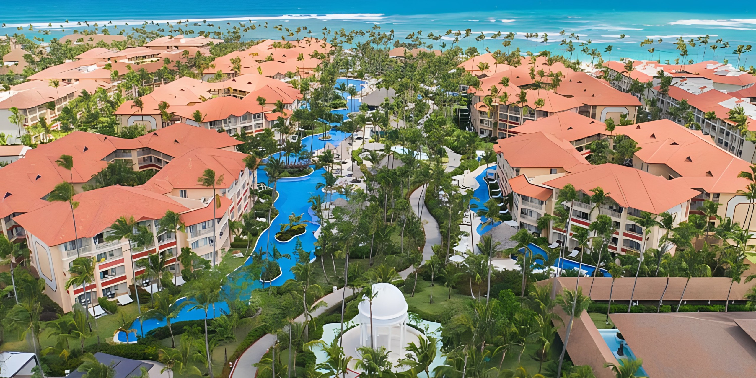 Aerial view of the Majestic Elegance Punta Cana resort with red-roofed buildings, winding pools, and lush greenery.