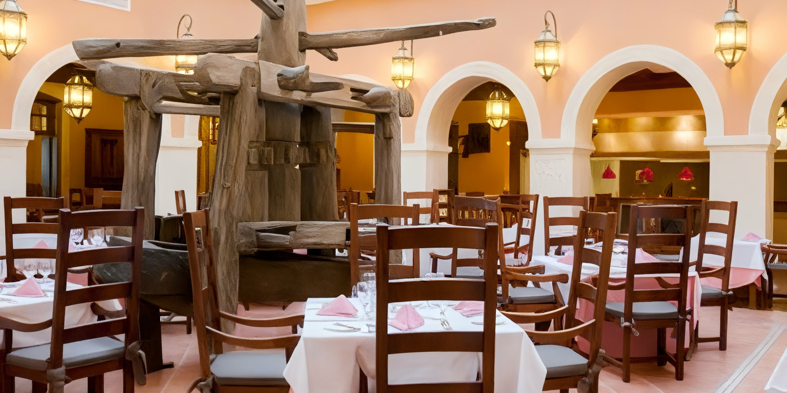 The interior of Majestic Elegance Punta Cana features wooden tables and chairs, pink table settings, arched doorways, and a large wooden sculpture in the center.