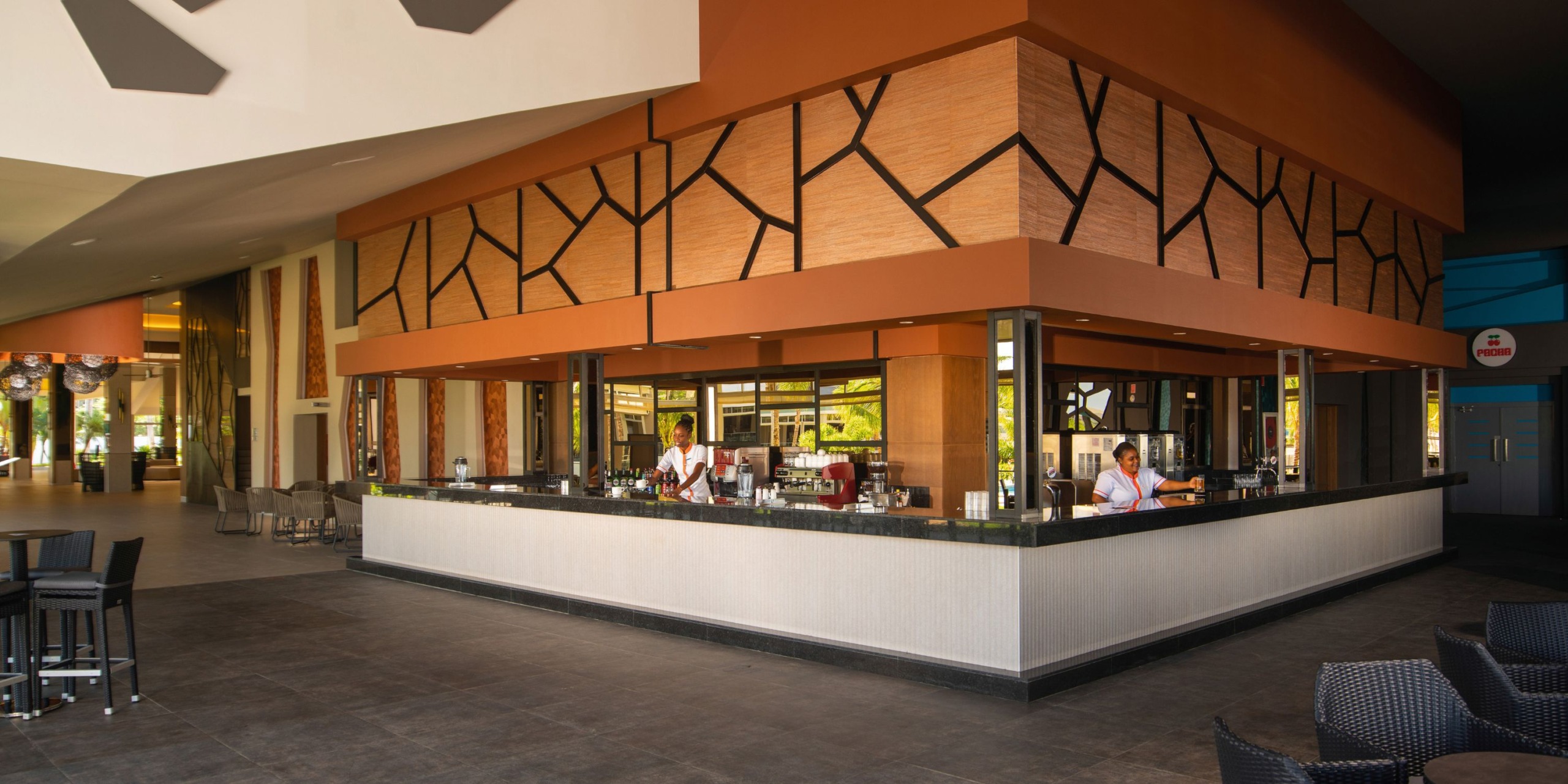 The lobby bar at Hotel Riu Montego Bay showcases a geometric design with a sleek black countertop and is staffed by two employees.