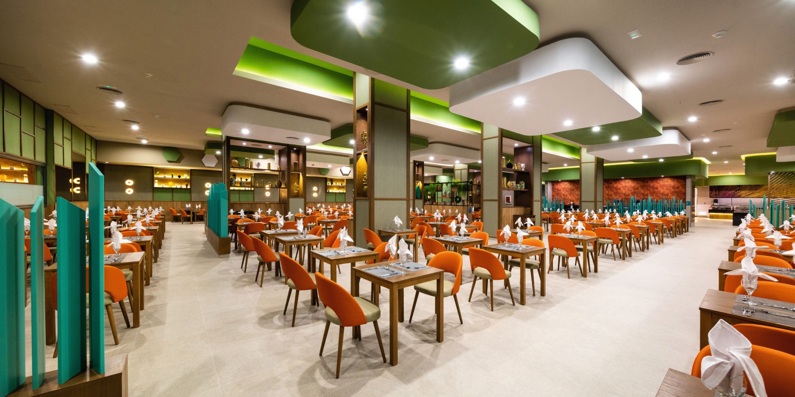 Hotel Riu Montego Bay is a spacious dining venue with orange chairs and neatly set tables, showcasing modern decor complemented by green accents on the walls and ceiling.