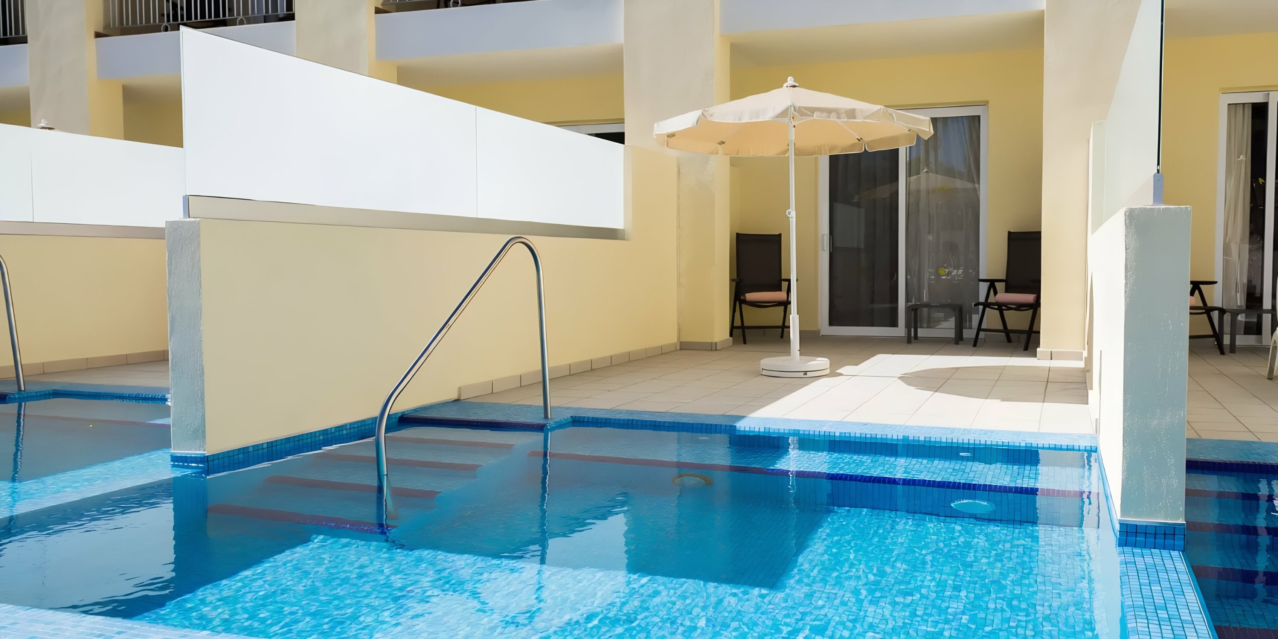 A poolside patio area with a blue swimming pool, white umbrella, and metal handrails at Hotel Riu Palace Cabo San Lucas.