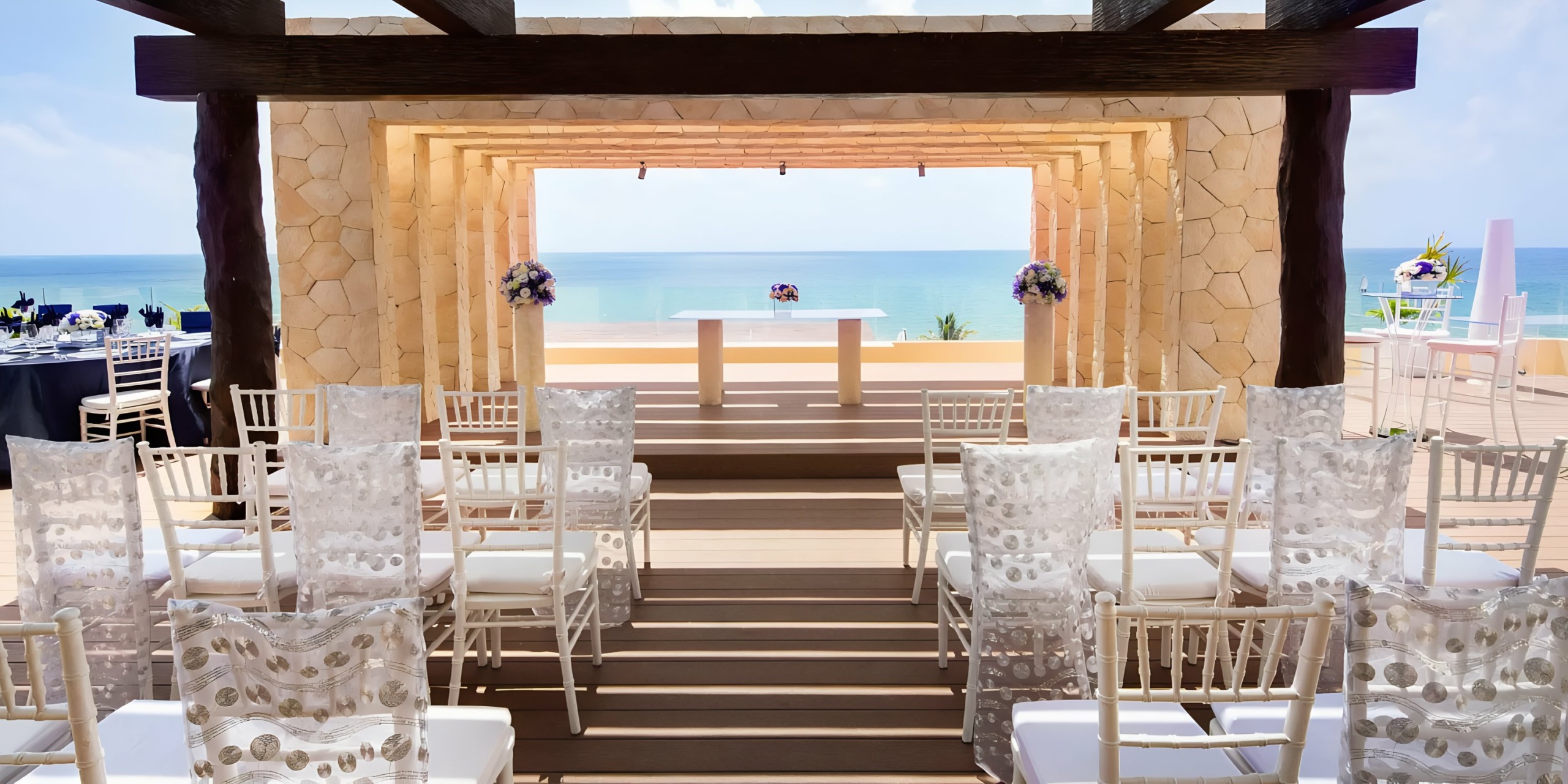 Beachfront Royalton Riviera Cancun wedding setup with white chairs and a wooden gazebo overlooking the ocean.