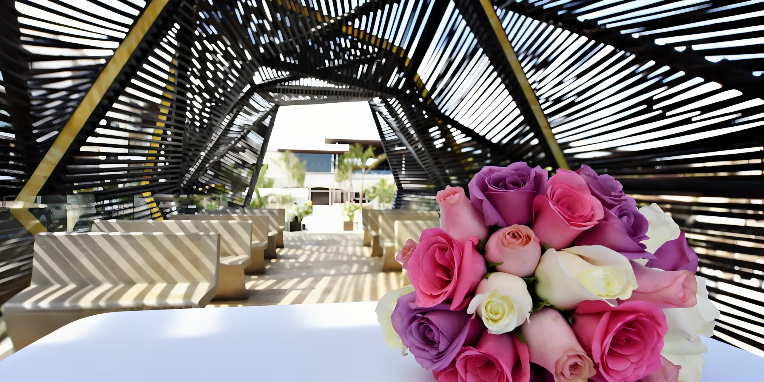 Bouquet of roses on a table at a Royalton Riviera Cancun wedding with geometric pergola and outdoor seating in the background.