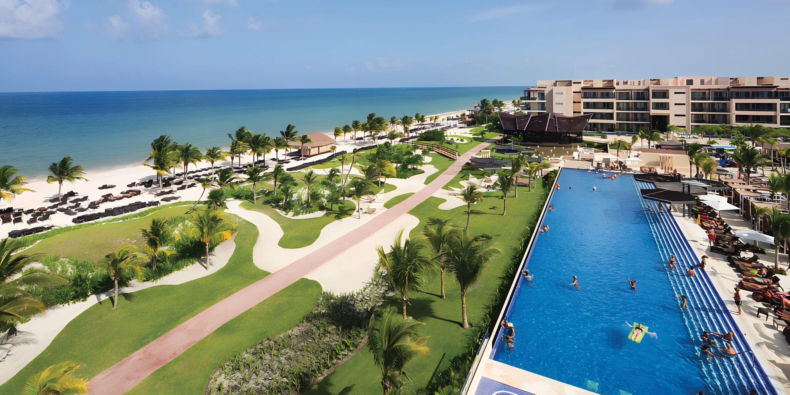 Royalton Riviera Cancun, a luxury beach resort with a large swimming pool, sun loungers, and palm trees along a sandy beach.
