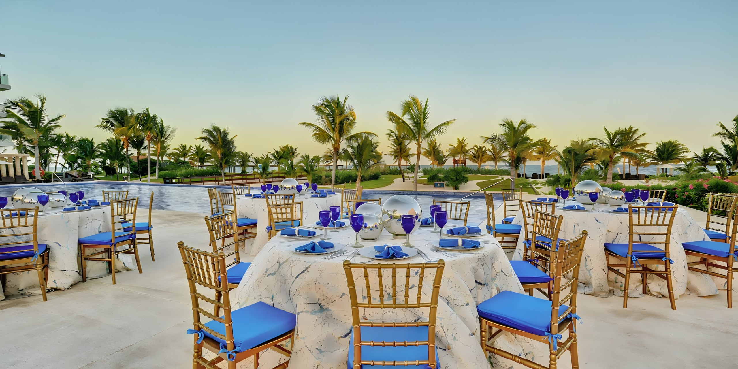 Outdoor dining setup with blue and white table settings at a Riviera Cancun wedding during sunset.
