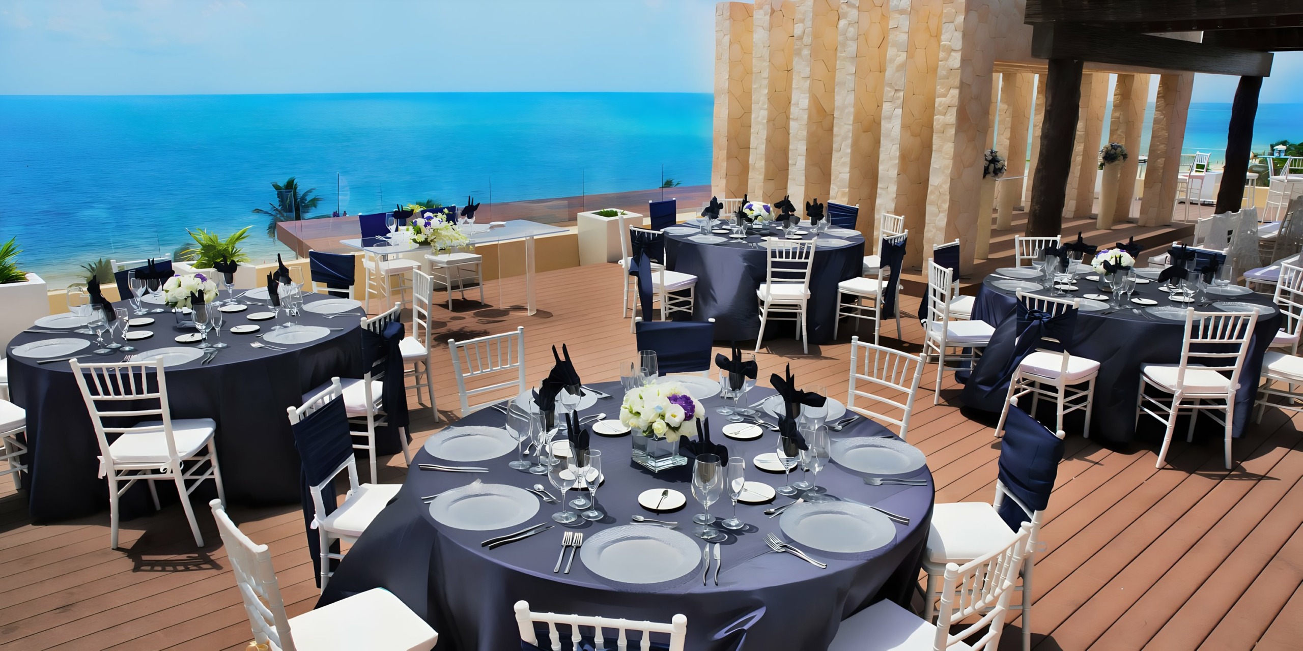 Outdoor dining setup by the sea with elegantly arranged tables and chairs for a Royalton Riviera Cancun wedding.