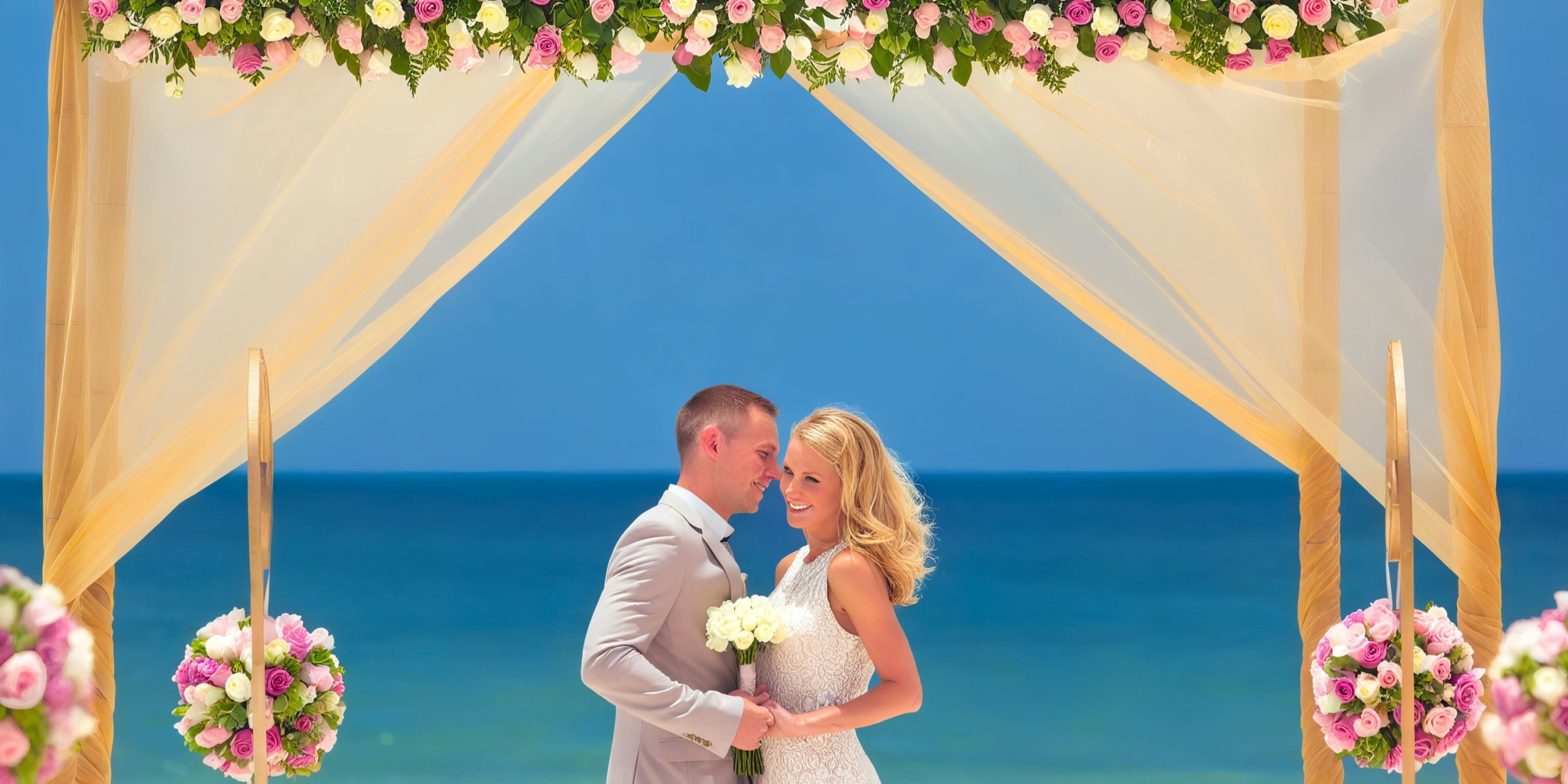 A couple stands under a floral wedding arch on the beach at the Royalton Riviera Cancun, with the sea and sky as their stunning backdrop.