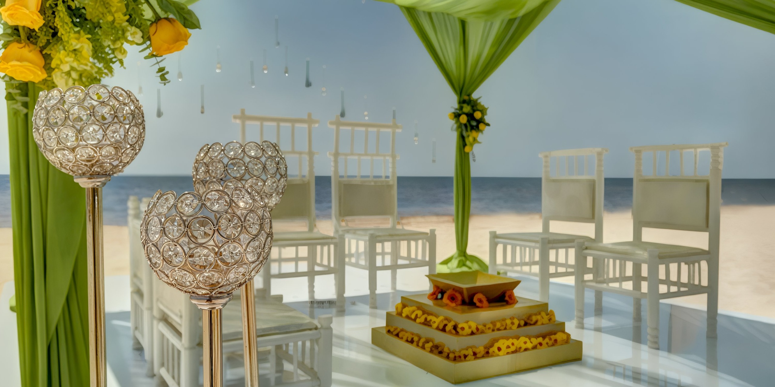 The stunning wedding setup at Royalton Riviera Cancun includes white chairs, sophisticated green drapes, and sparkling crystal decorations. At its center, a tiered platform embellished with vibrant flowers provides breathtaking ocean views.