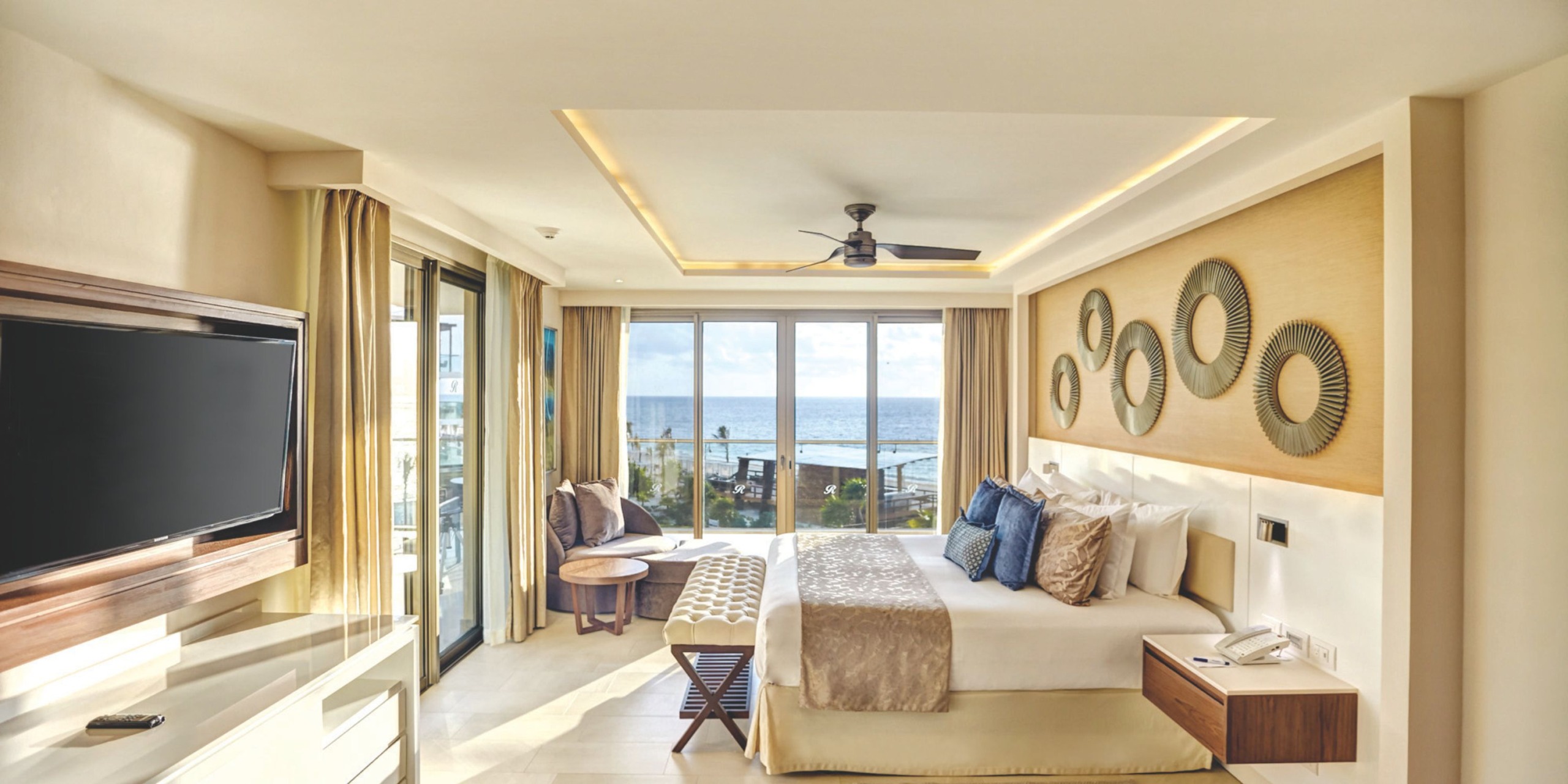 Indulge in the ultimate luxury and romance at Royalton Riviera Cancun, where your hotel room boasts a king-sized bed, stunning decorative wall art, a TV, and a comfortable seating area. Enjoy breathtaking ocean views through expansive windows, making it the perfect retreat for your wedding celebration.