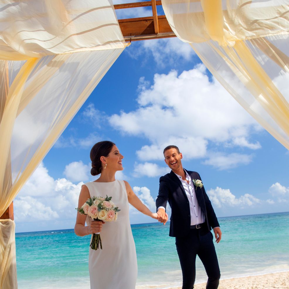 Newlweds holding hands under canopy at destination beach wedding at Royalton Bavaro Resort & Spa Punta Cana Dominican Republic