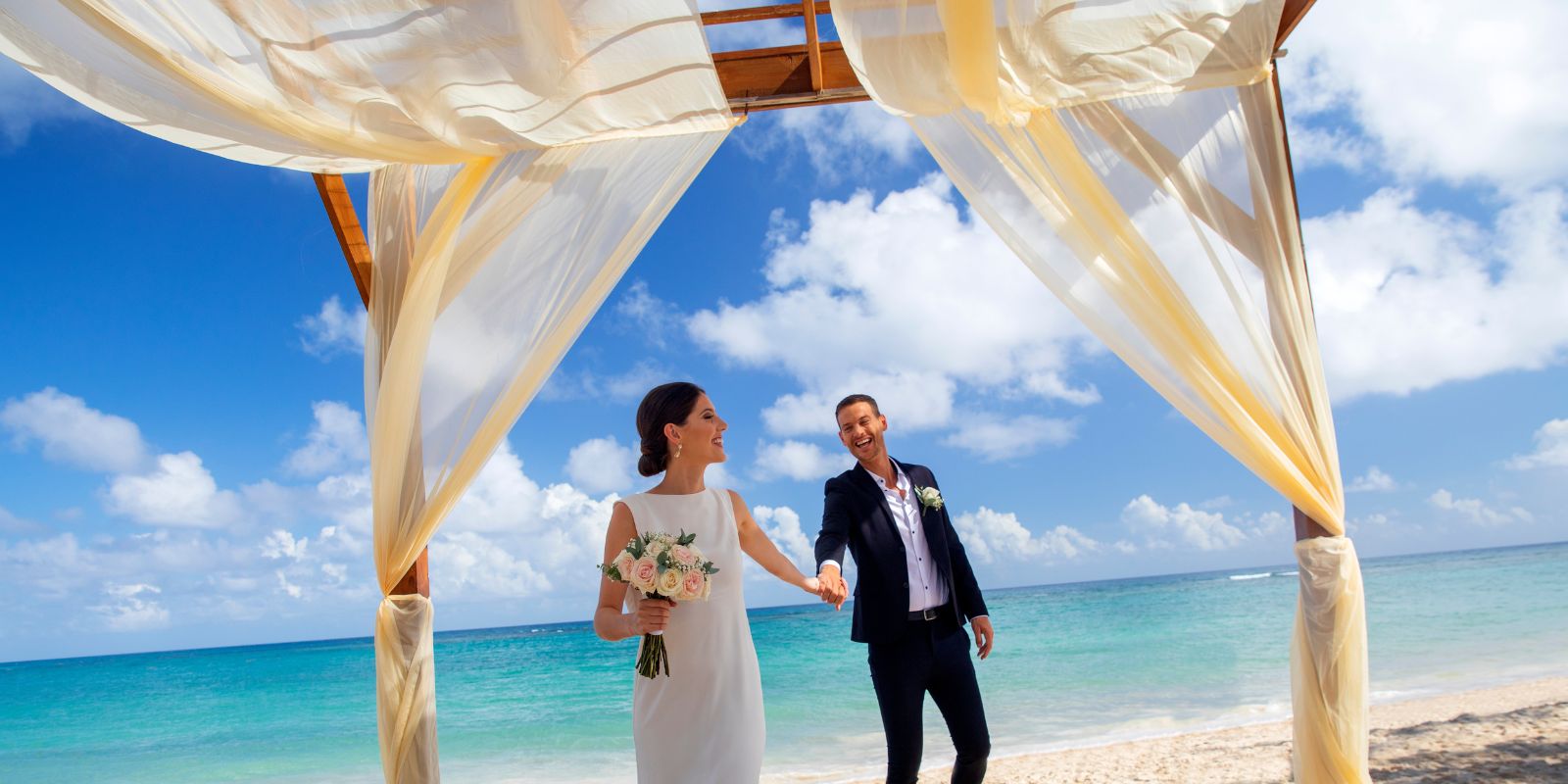 Newlweds holding hands under canopy at destination beach wedding at Royalton Bavaro Resort & Spa Punta Cana Dominican Republic