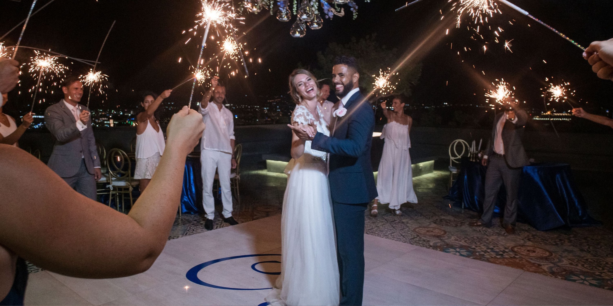 At Sandos Finisterra Los Cabos, a bride and groom dance surrounded by guests holding sparklers, with a nighttime backdrop and decorative lights above.