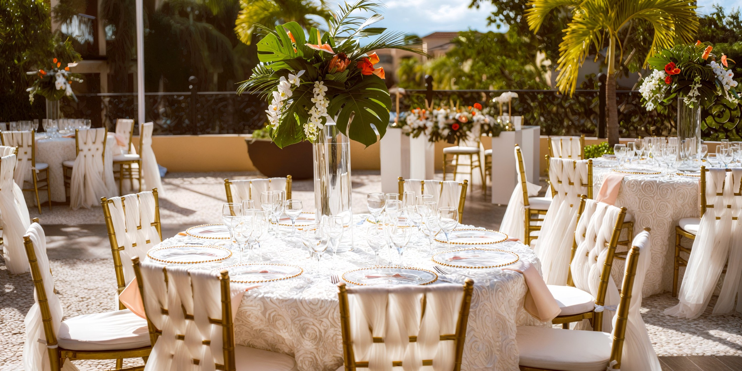 For a destination wedding at Sandos Playacar, the event is elegantly arranged with round tables adorned with floral centerpieces and complemented by white chairs.