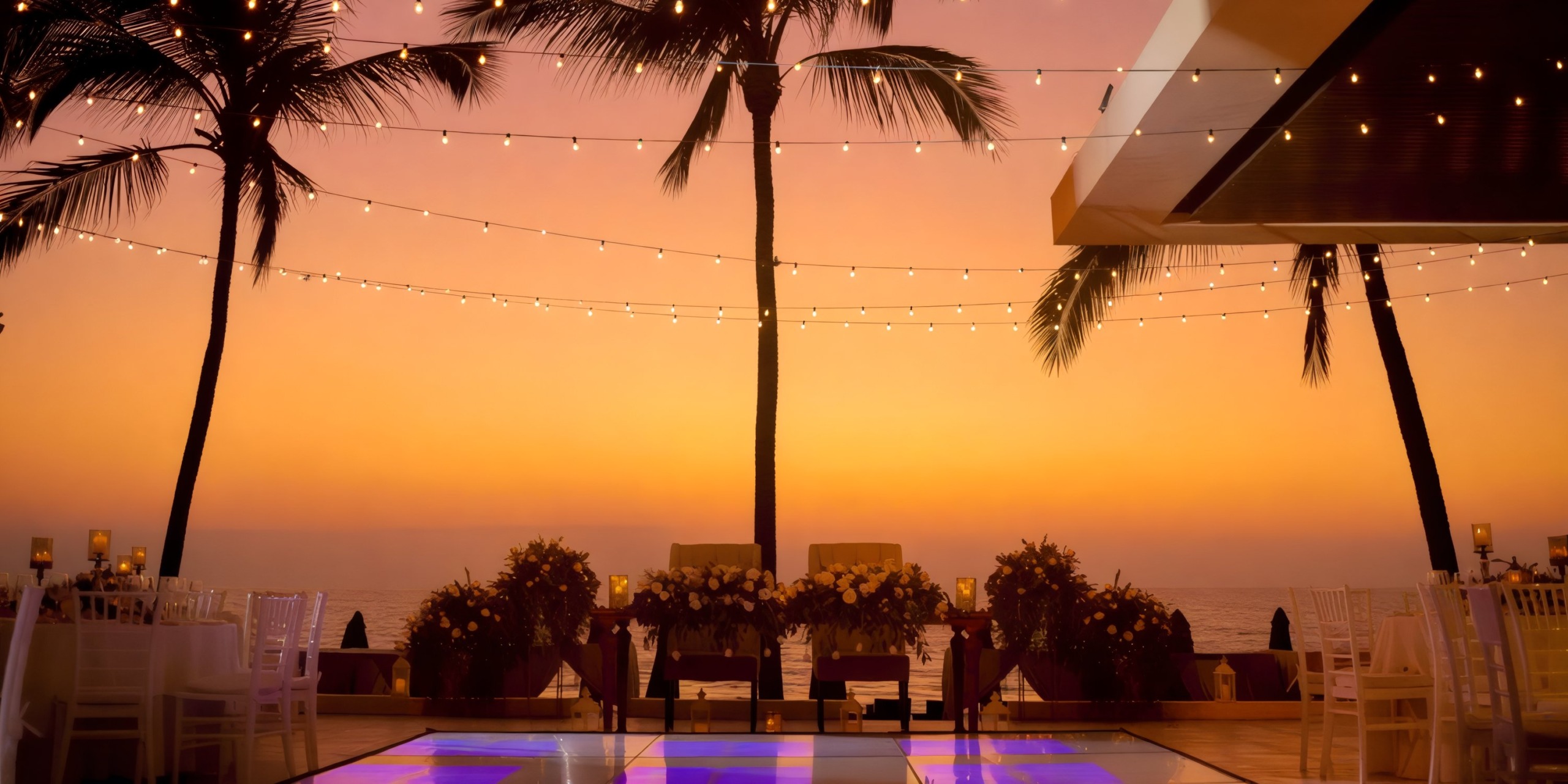 Experience a breathtaking sunset view perfect for a destination wedding at Marival Emotions, where palm trees sway and string lights twinkle above beautifully decorated oceanfront tables.