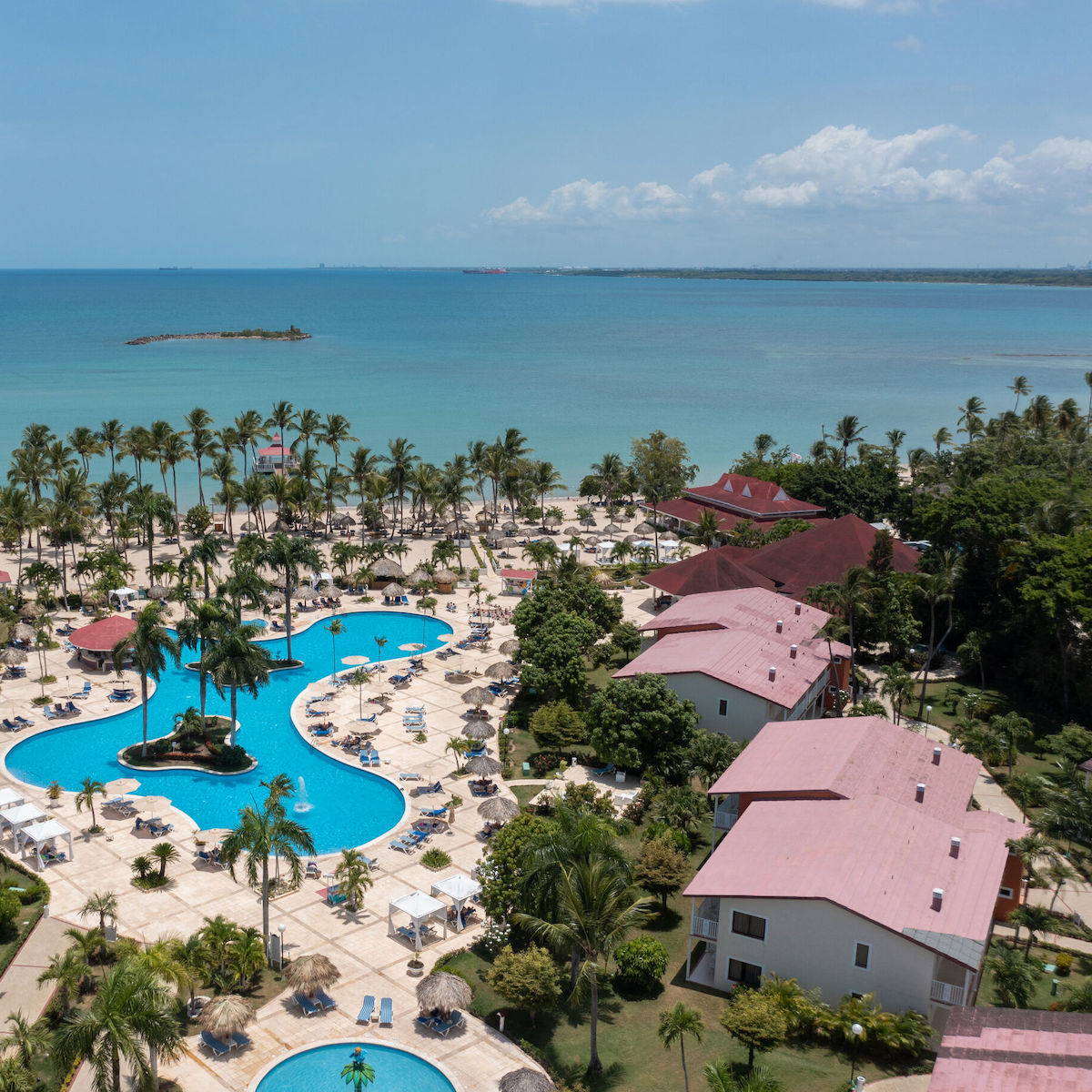 Aerial view of Bahia Principe Grand La Romana showcases a stunning setting for a destination wedding, featuring inviting pools and lush palm trees with an ocean backdrop.