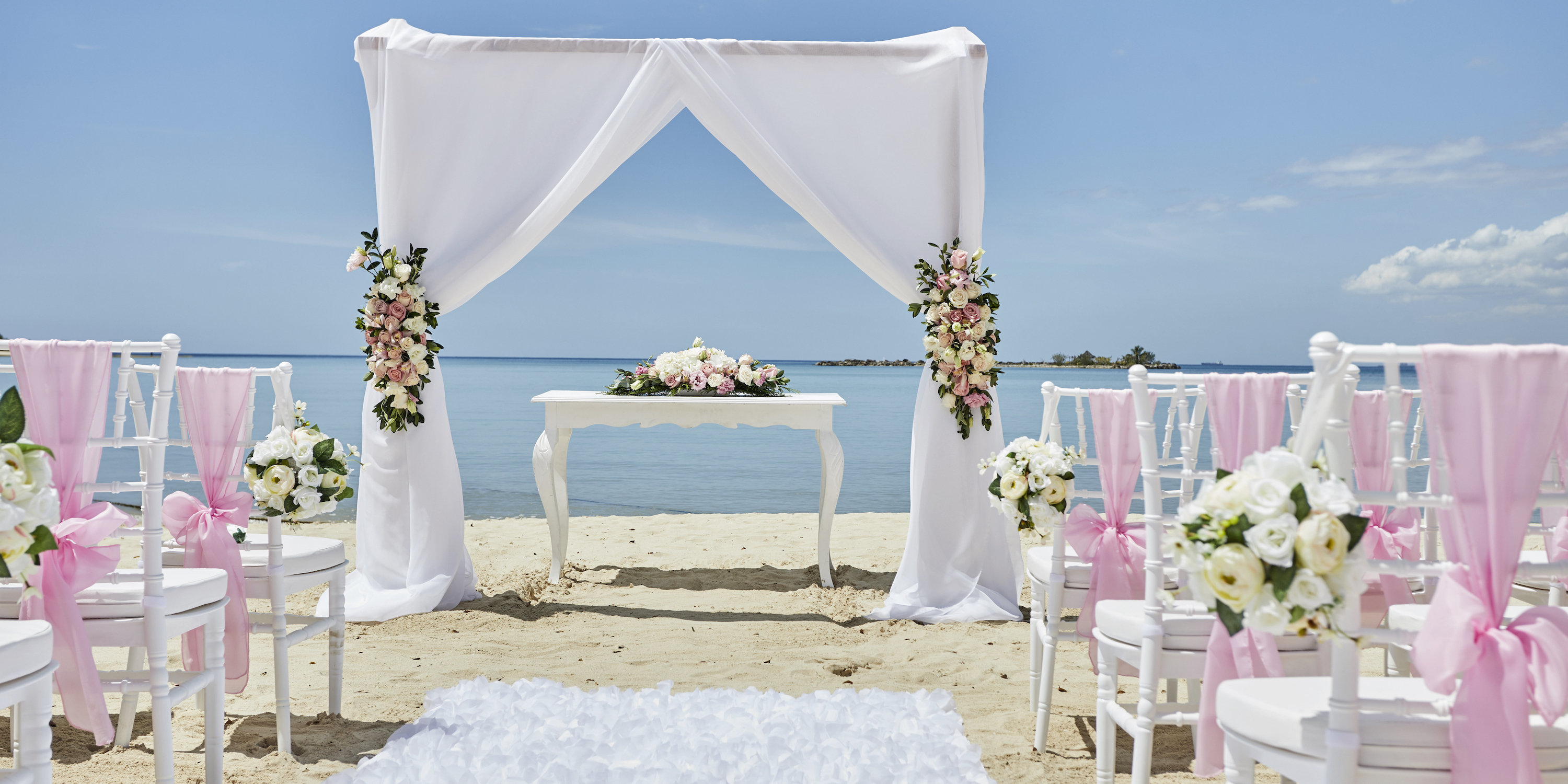 Bahia Principe Grand La Romana's beach is beautifully arranged for a destination wedding, featuring white chairs, floral decor, and a charming sea-side arch.