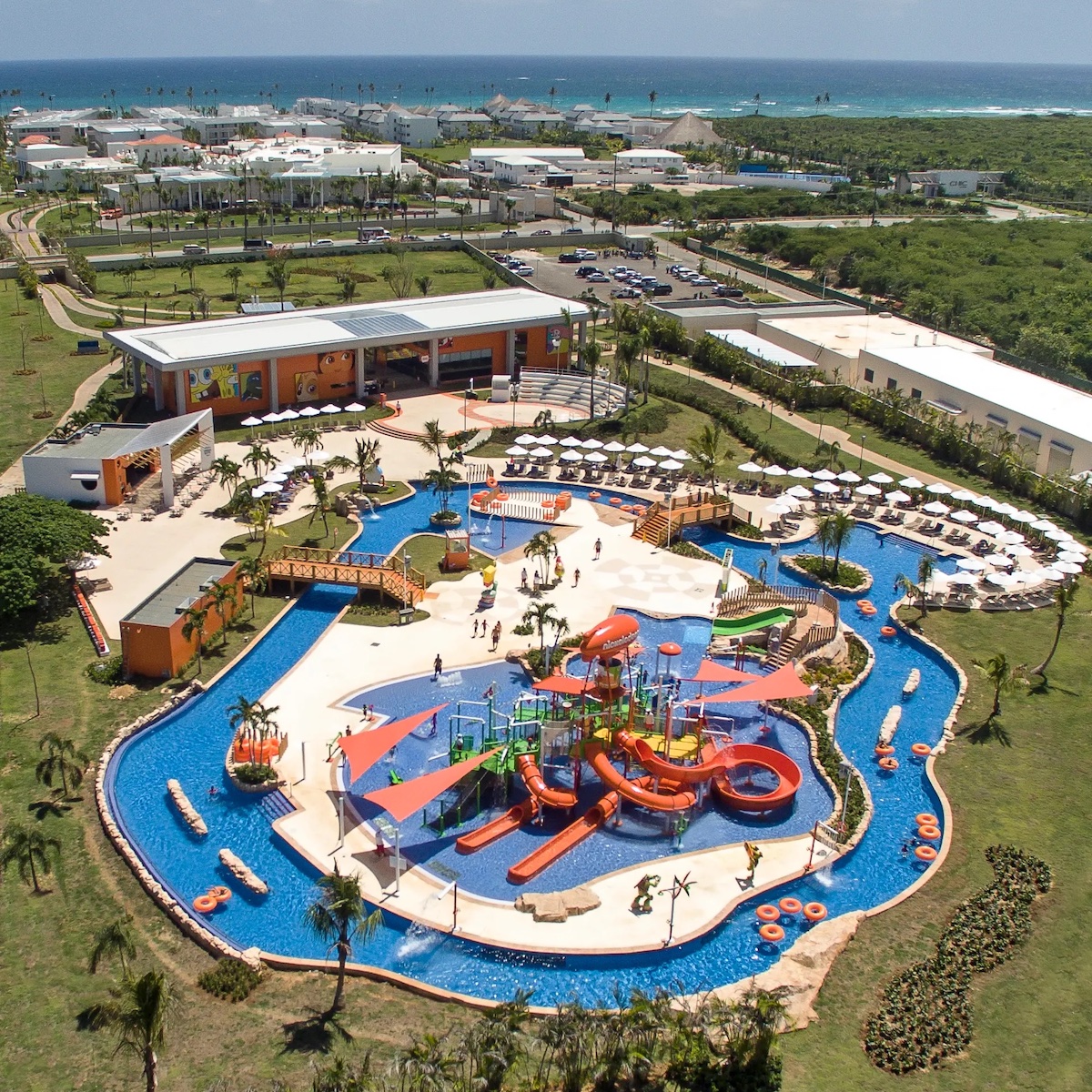 Aerial view of Nickelodeon Hotels & Resorts Punta Cana with vibrant slides and play areas surrounded by pavilions and greenery near a coastal area, perfect for a destination wedding.