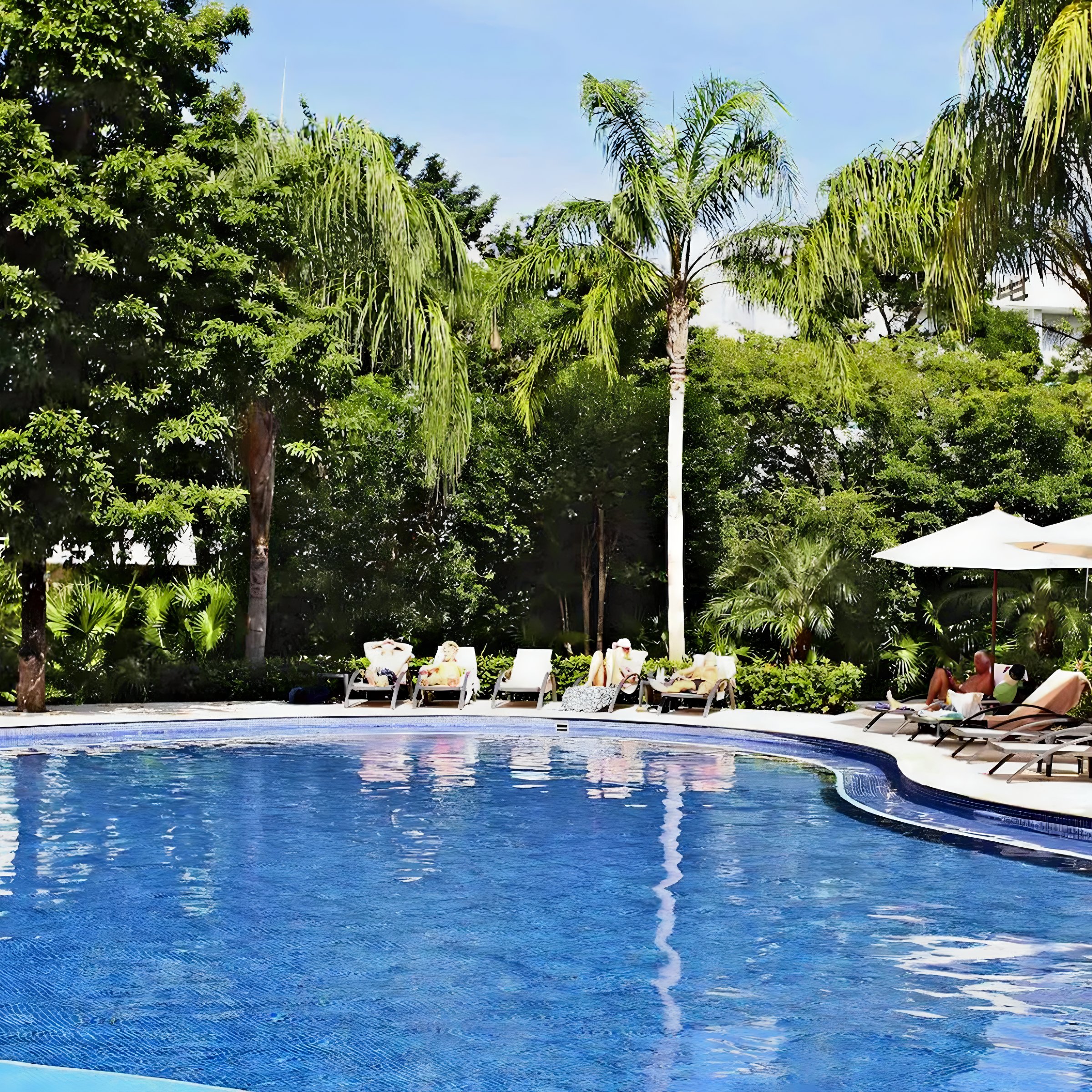 People lounging by a crystal blue pool at all inclusive resort Bahia Principe Luxury Sian Ka'an