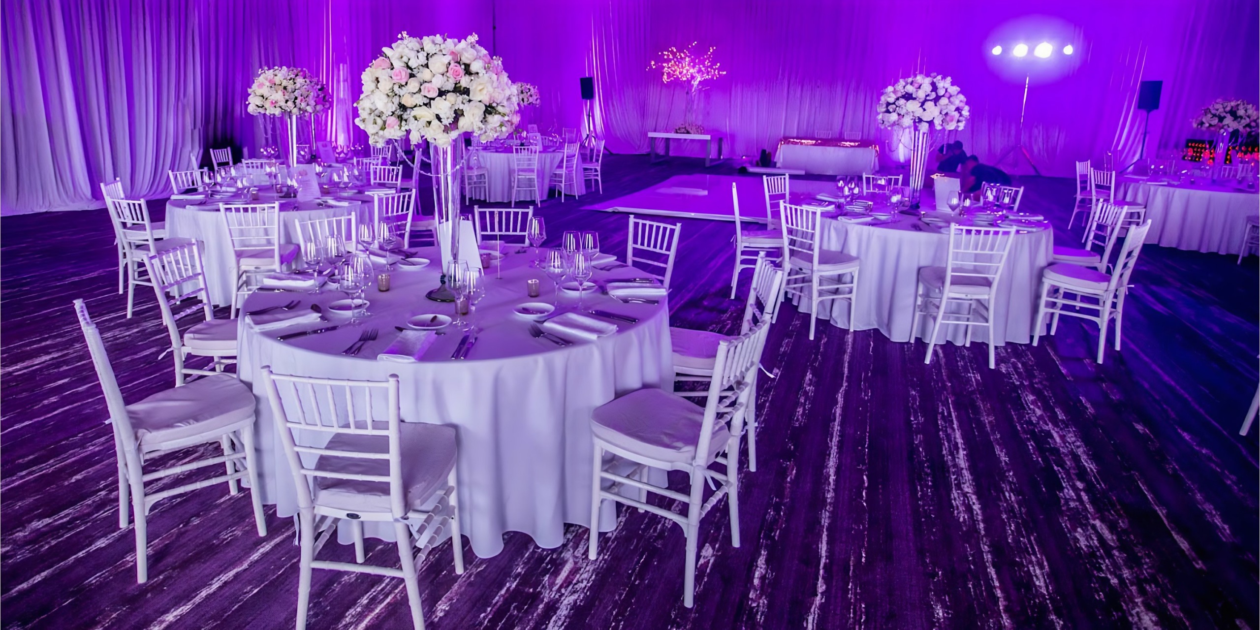 A wedding reception set up at Breathless Riviera Cancún Resort & Spa with white tables and purple lighting.