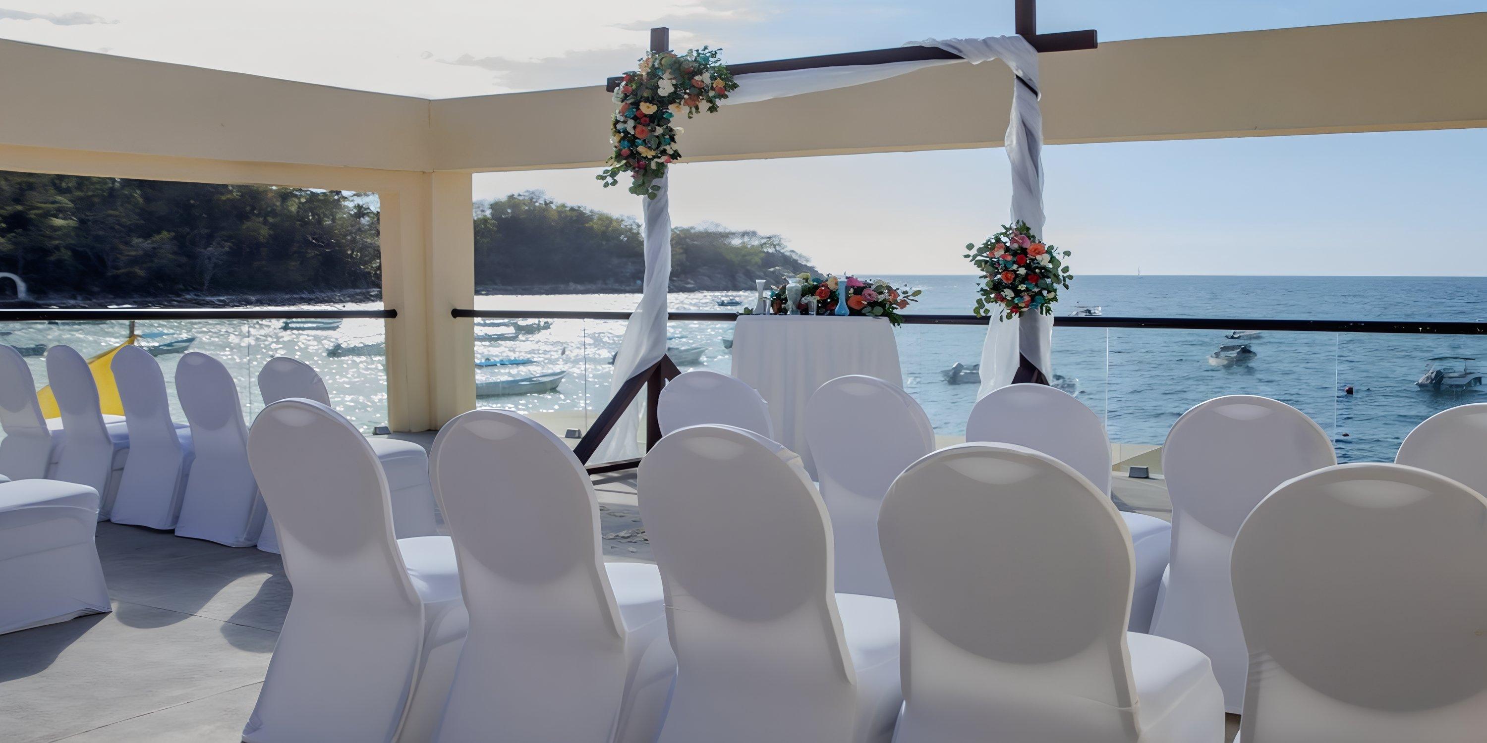 White chairs face a floral arch arranged for a destination wedding by the sea at Barcelo Puerto Vallarta.