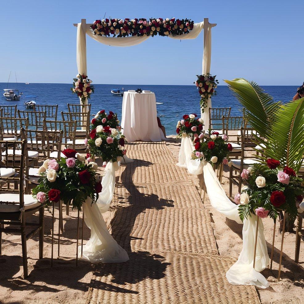 Destination wedding setup on the beach with chairs, floral decor, and an arch overlooking the ocean.