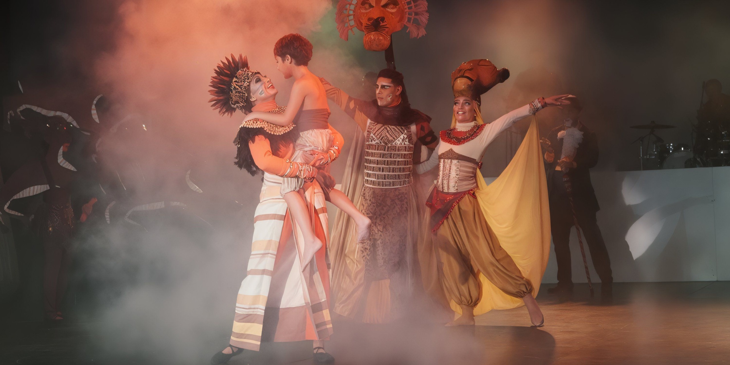 At Catalonia Playa Maroma, performers in elaborate costumes engage in a theatrical scene with dramatic lighting and smoke effects on stage.