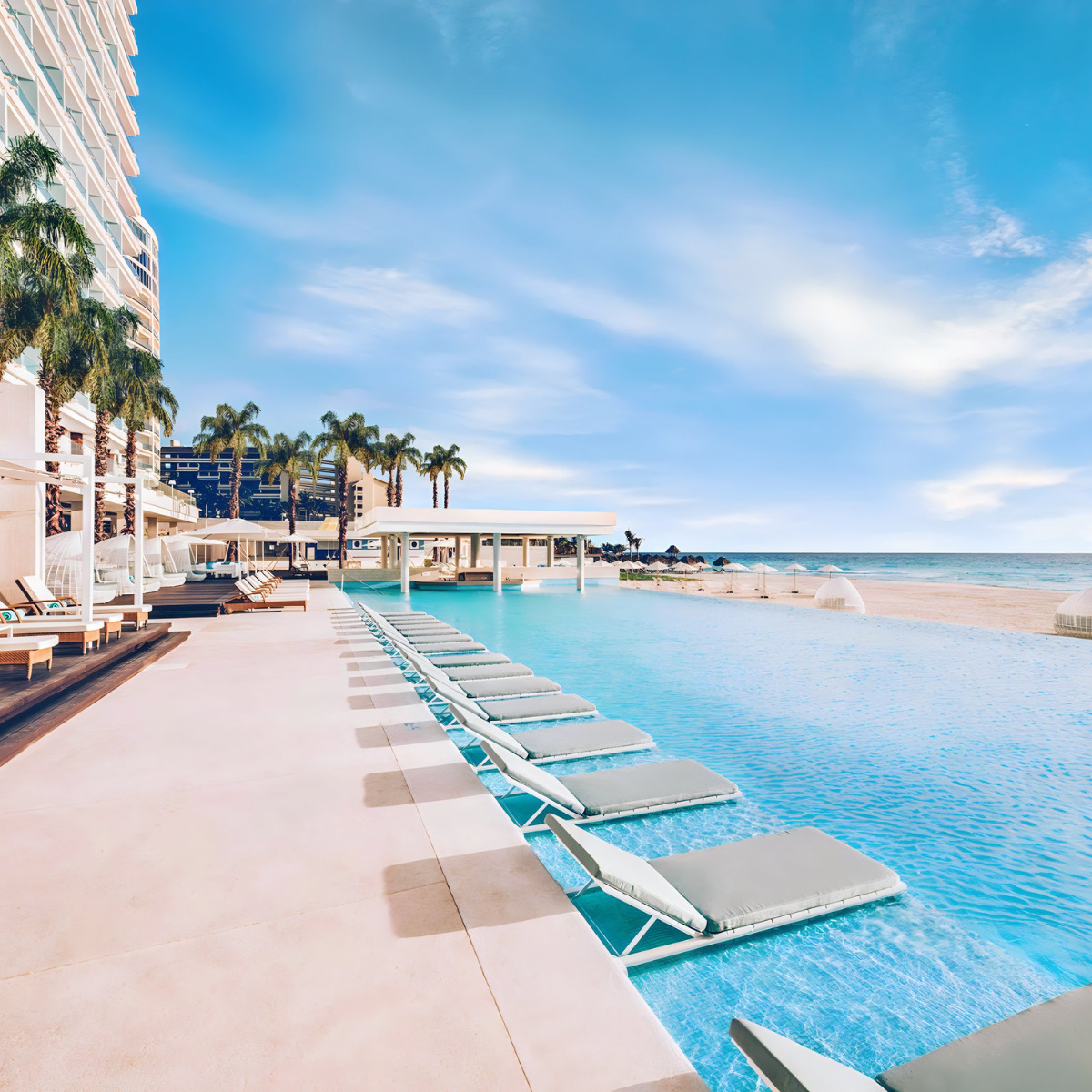A large swimming pool with lounge chairs on the beach, perfect for a destination wedding at the Coral Level at Iberostar Selection Cancun.